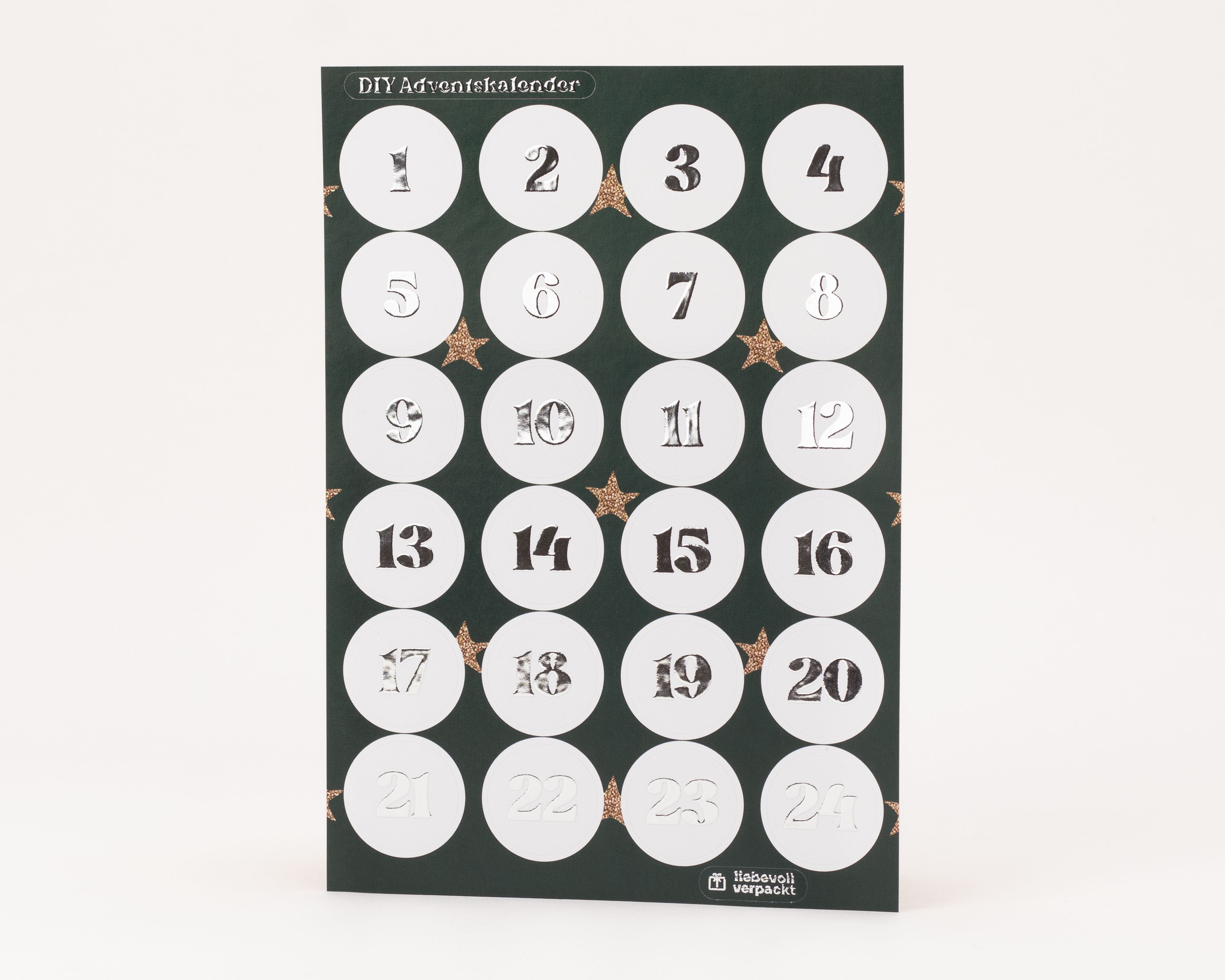 Eleganter Stickerbogen für einen DIY-Adventskalender mit 24 runden, weißen Aufklebern. Die Zahlen 1 bis 24 sind mit glänzender Silberfolie veredelt und heben sich vom dunkelgrünen Trägerpapier ab.