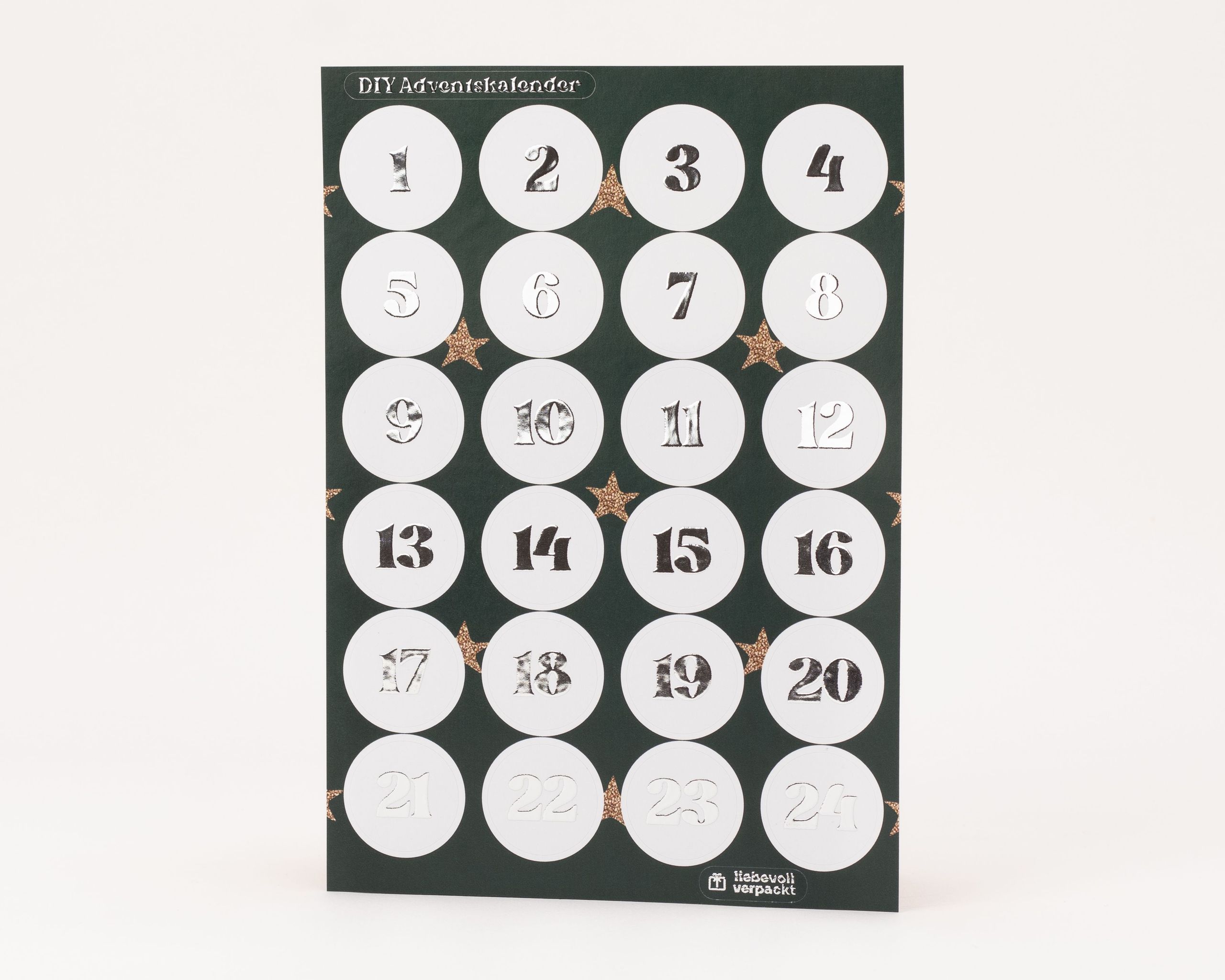 Eleganter Stickerbogen für einen DIY-Adventskalender mit 24 runden, weißen Aufklebern. Die Zahlen 1 bis 24 sind mit glänzender Silberfolie veredelt und heben sich vom dunkelgrünen Trägerpapier ab.