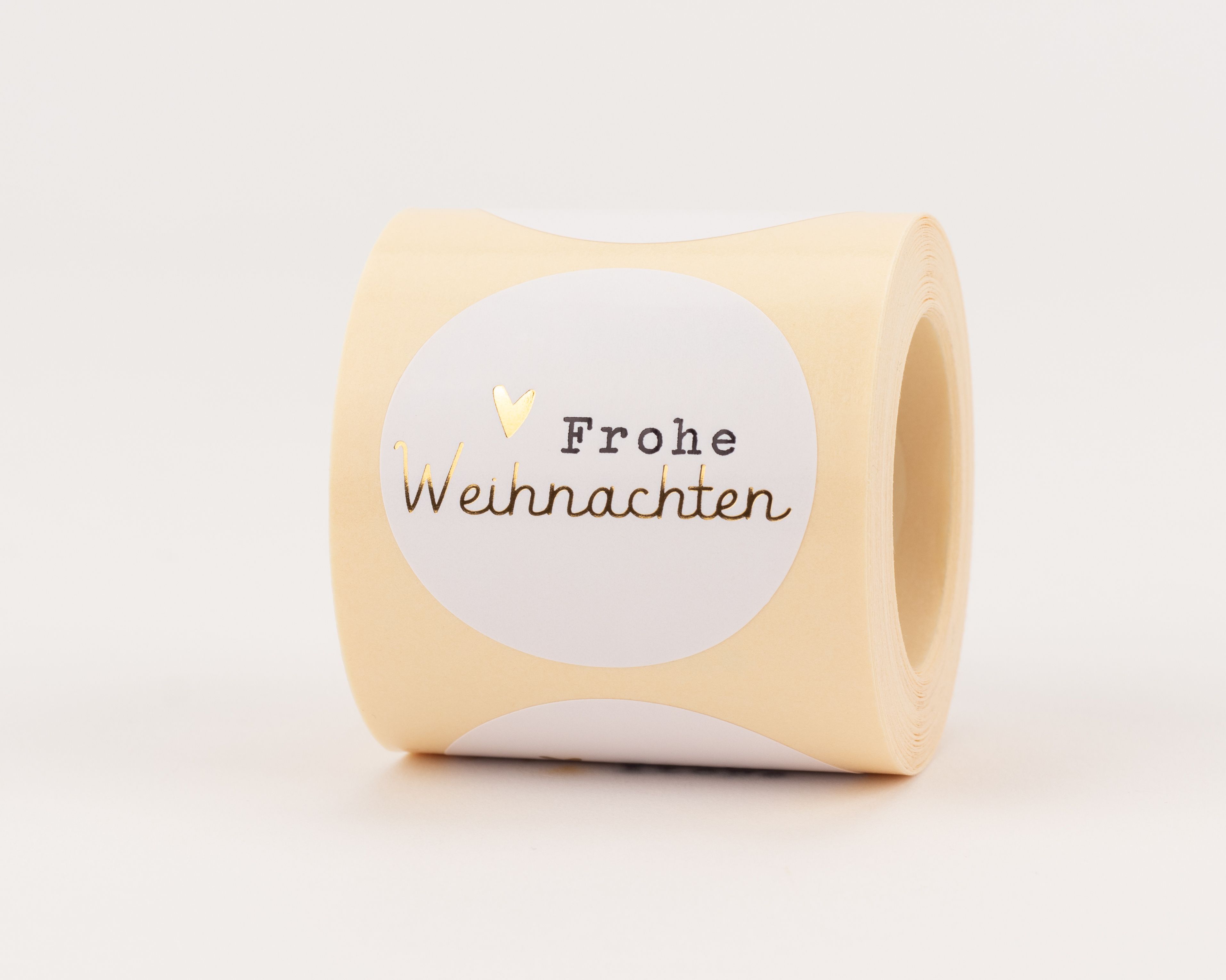Aufkleber mit rundem Design, weißem Zentrum und beigem Rand. Sie zeigen 'Frohe Weihnachten' in Schwarz und Gold-Effekt, dazu ein goldenes Herz