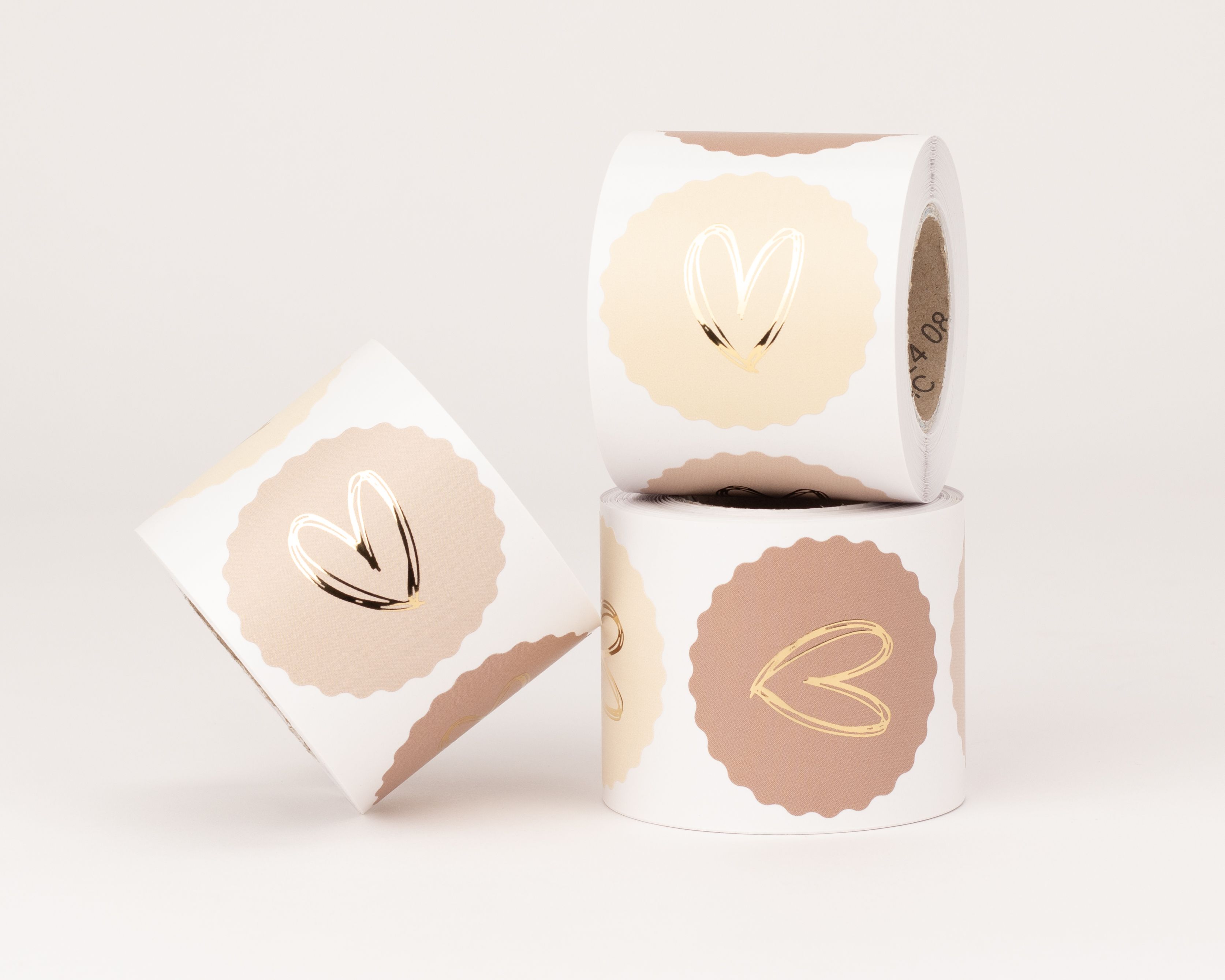 Aufkleber zeigen drei verschiedene Designs mit goldfarbenem Herz Motiv auf rosa und beigefarbenem Hintergrund