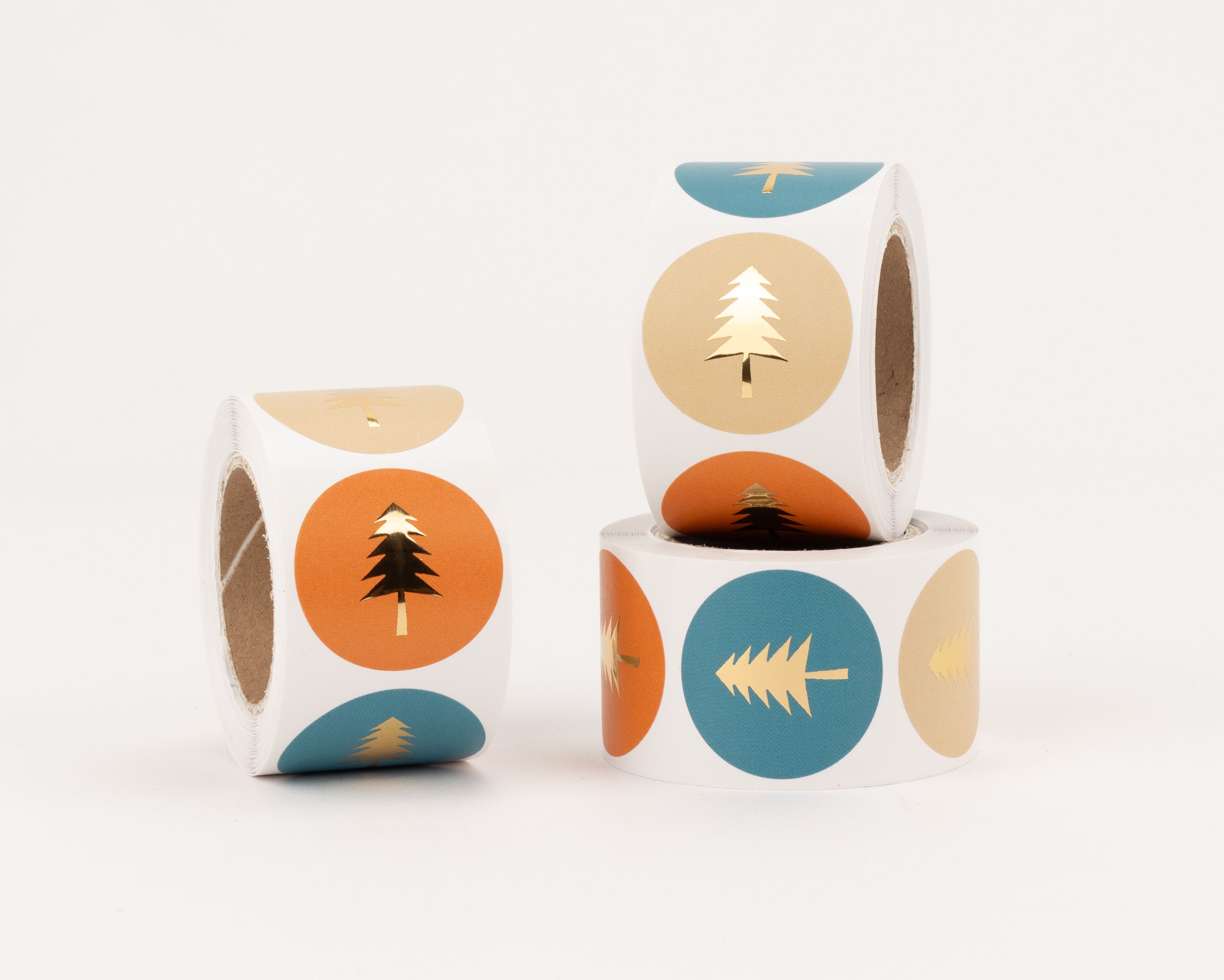 Aufkleber mit runden Tannenbaum-Motiven in Rost, Beige und Petrol, jeweils mit glänzendem Gold-Effekt. Das Set bietet drei verschiedene Designs