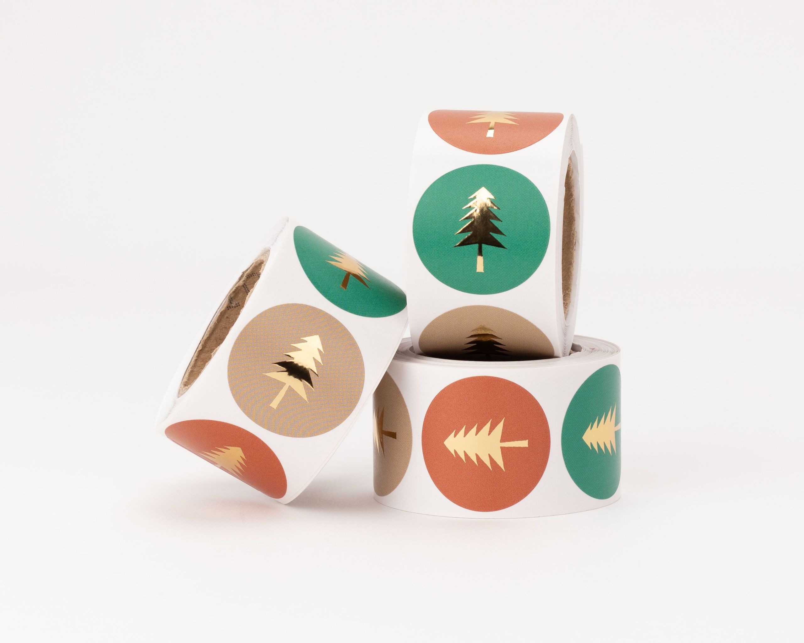 Aufkleber mit Tannenmotiv in drei verschiedenen Designs, jeweils mit goldfarbenem Baum auf rotem, grünem und taupefarbenem Hintergrund