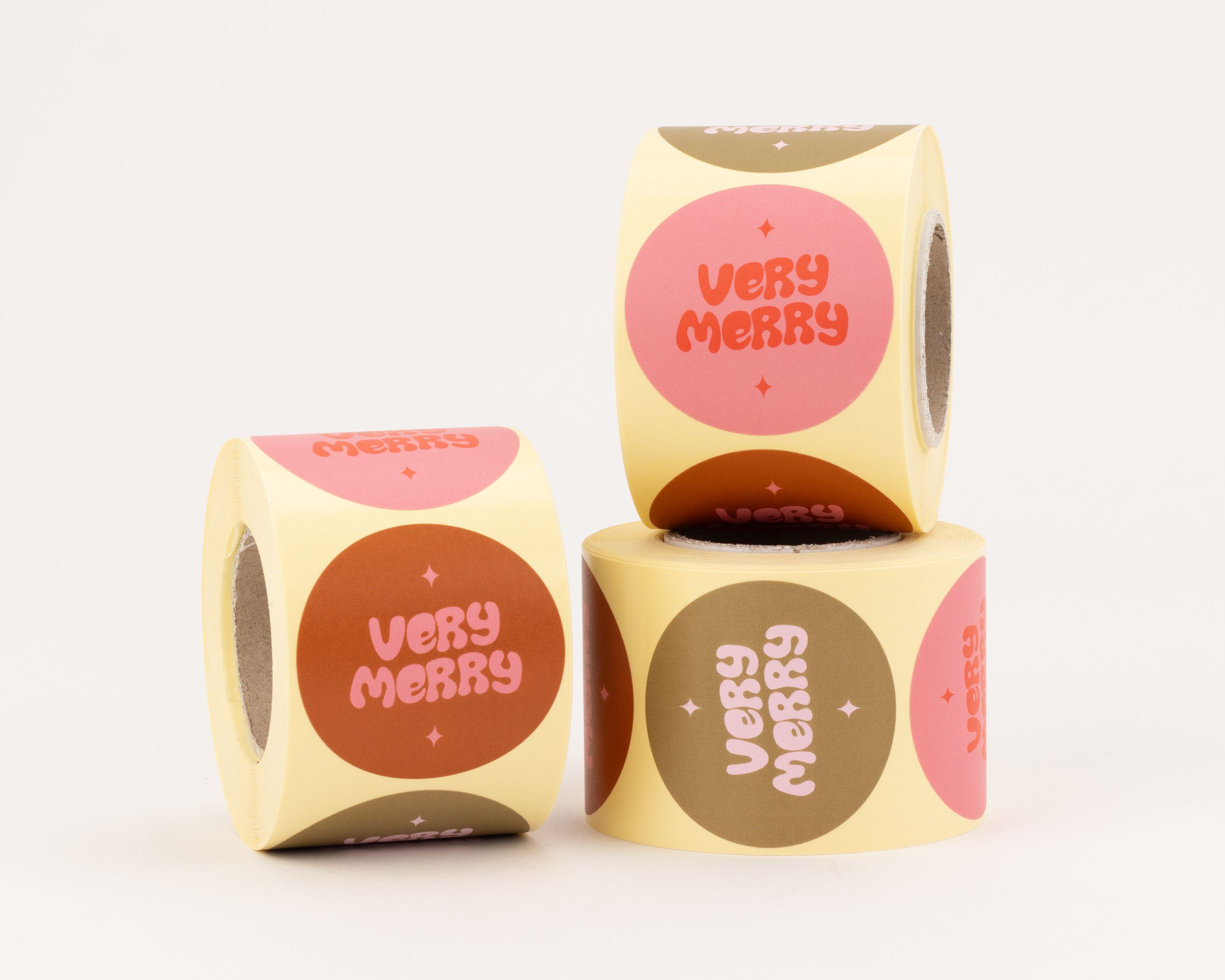 Aufkleber mit drei verschiedenen Very Merry Designs, die orange Schrift auf pinken und braunen Kreisen zeigen. Die runden Sticker enthalten kleine sternähnliche Akzente