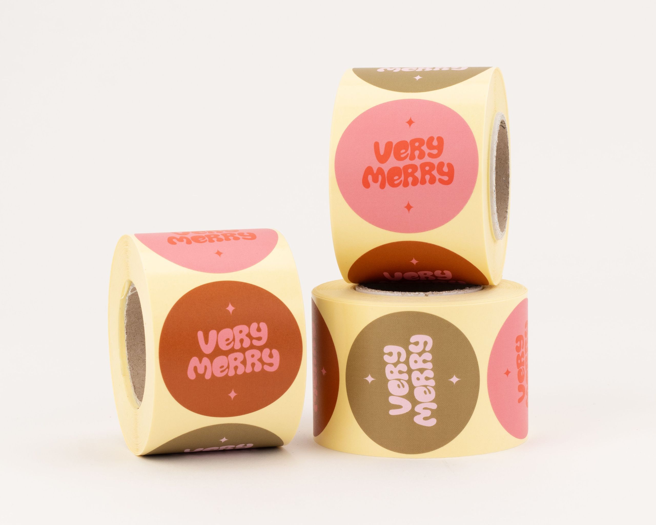 Aufkleber mit drei verschiedenen Very Merry Designs, die orange Schrift auf pinken und braunen Kreisen zeigen. Die runden Sticker enthalten kleine sternähnliche Akzente