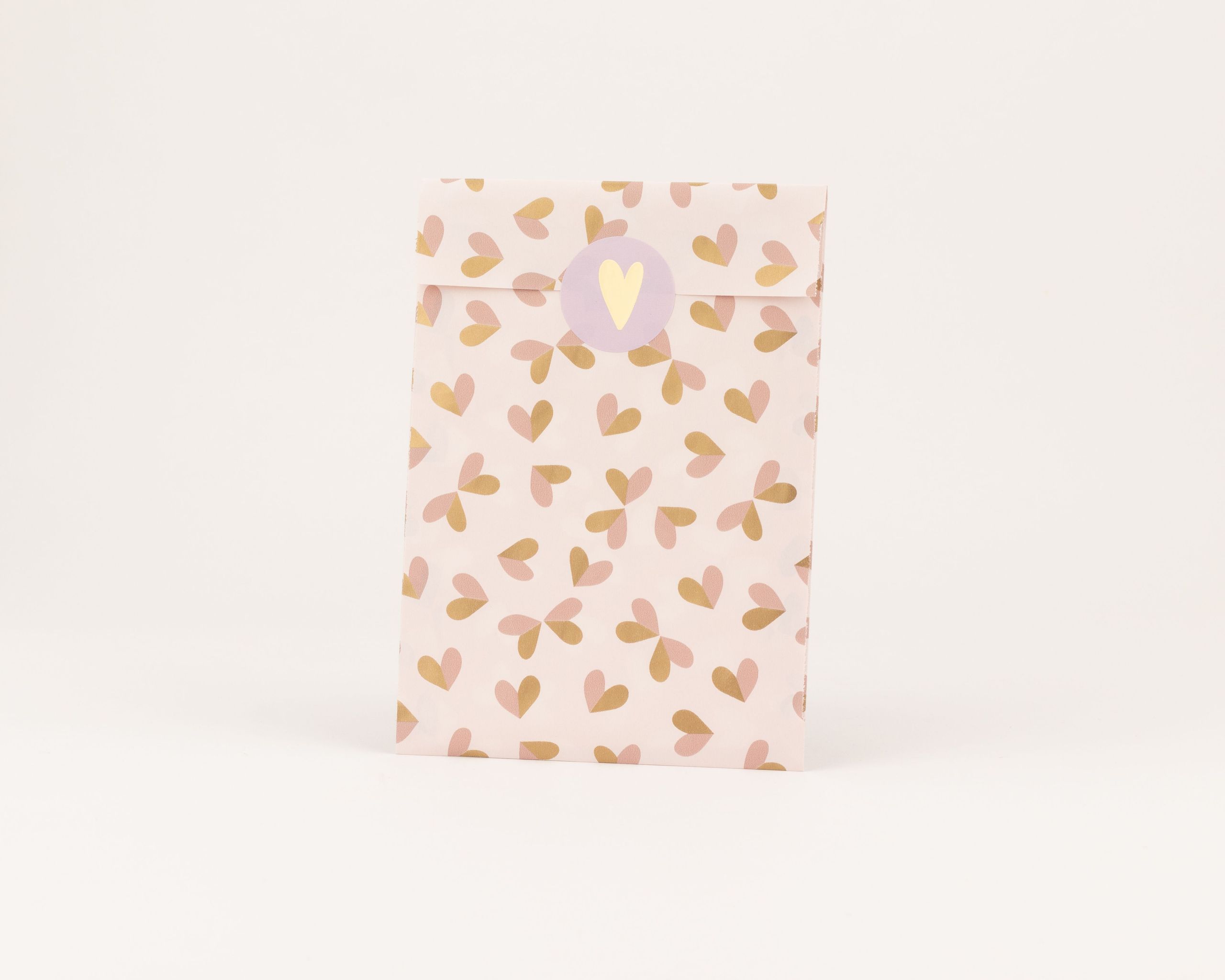 Papiertüten in Hellrosa mit Herzmuster in Rostbraun und Beige. Die Flachbeutel sind mit einem runden Aufkleber mit Herzmotiv geschlossen