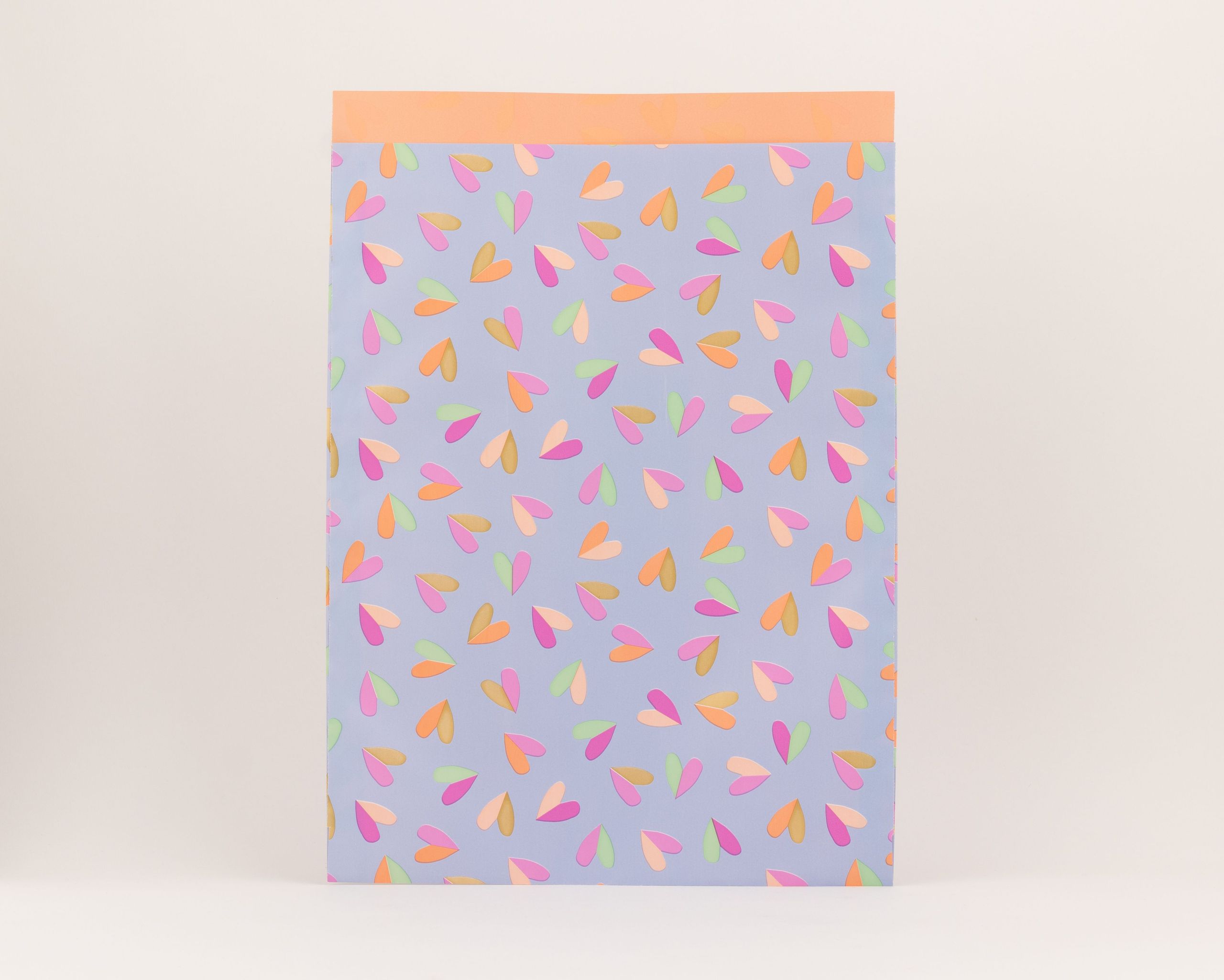 Flachbeutel mit blauem Hintergrund und einem Herzflatter-Muster in den Farben Pink, Grün, Orange und Gold. Die Innenseite ist einfarbig Orange