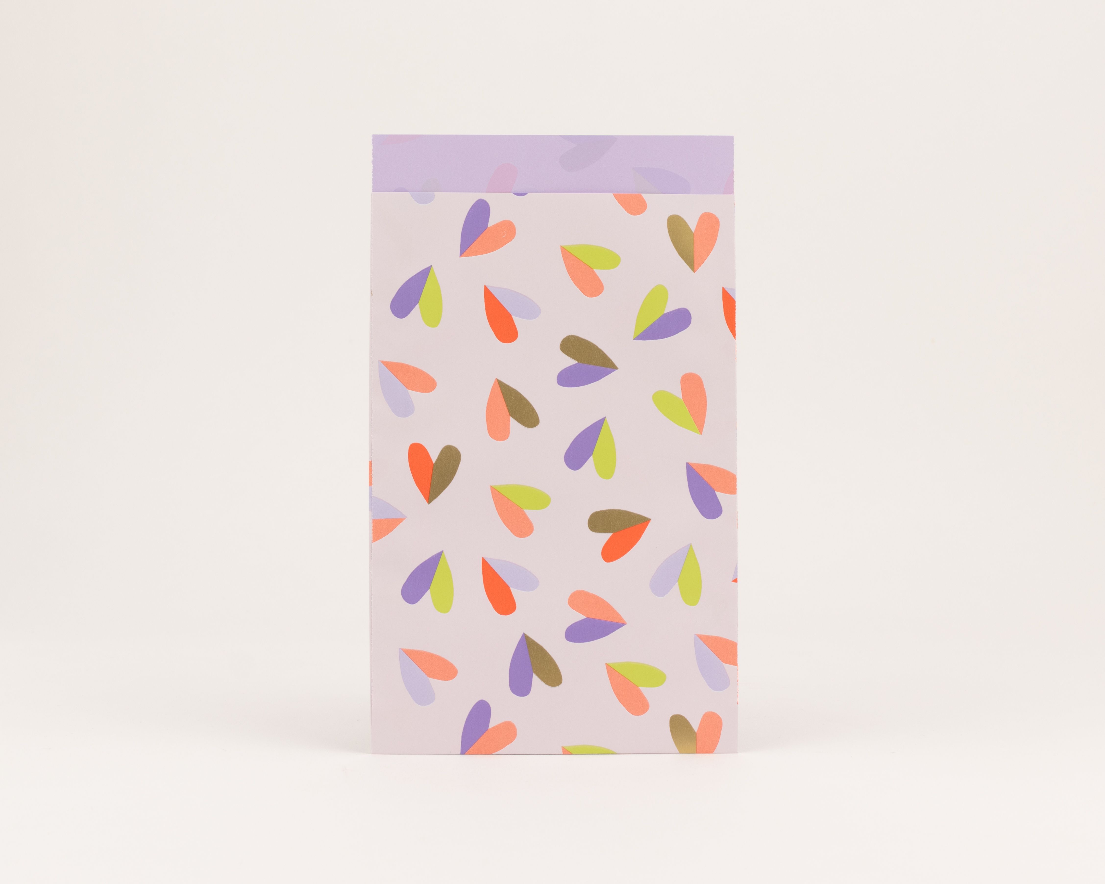 Flachbeutel zeigen ein Herzflatter-Muster auf hellviolettem Grund, mit Herzen in Orange, Violett und Limettengrün. Die Innenseite ist Fliederfarben