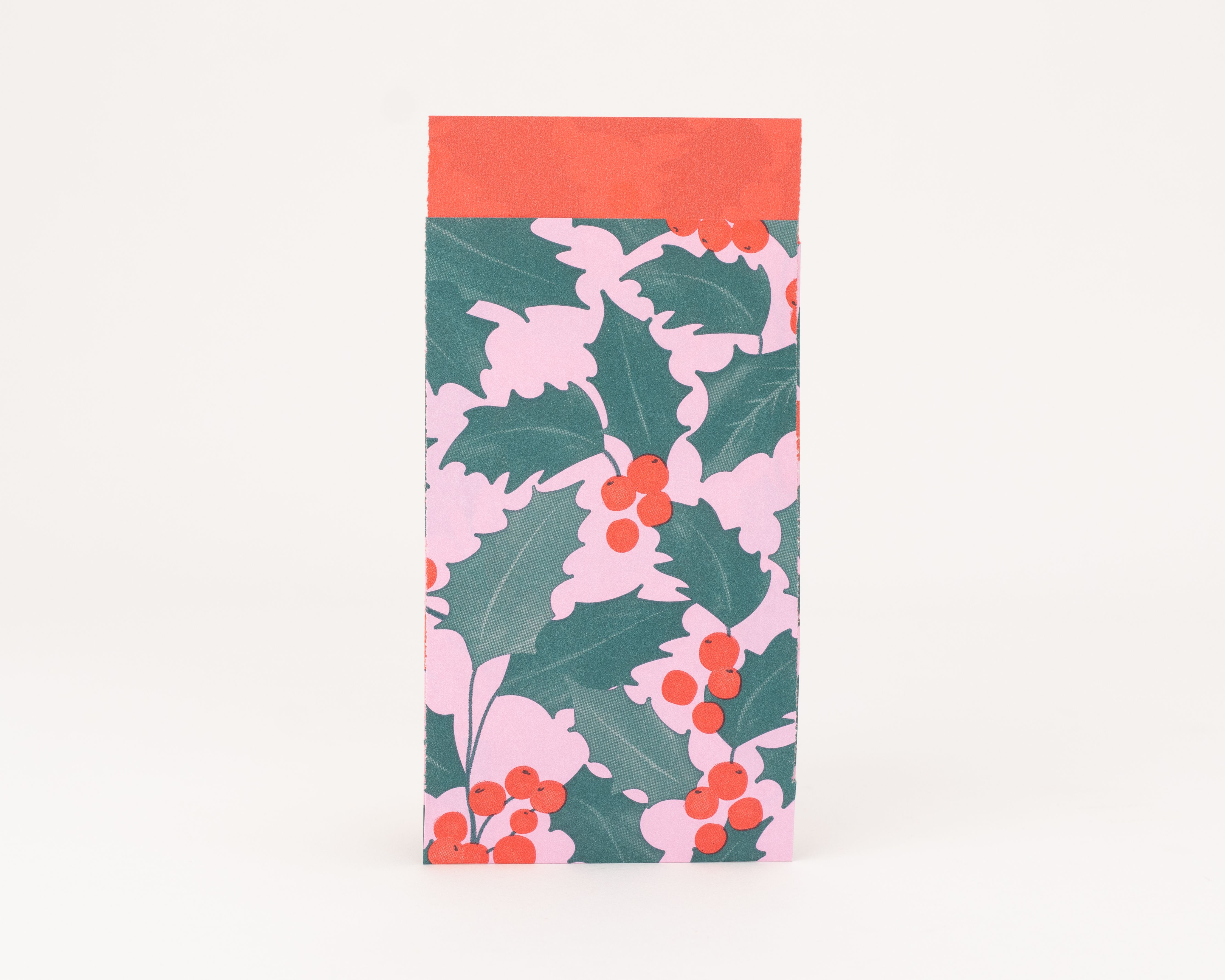 Flachbeutel mit einem rosa Muster aus grünen Ilexblättern und roten Beeren auf der Außenseite Die Innenseite ist rot