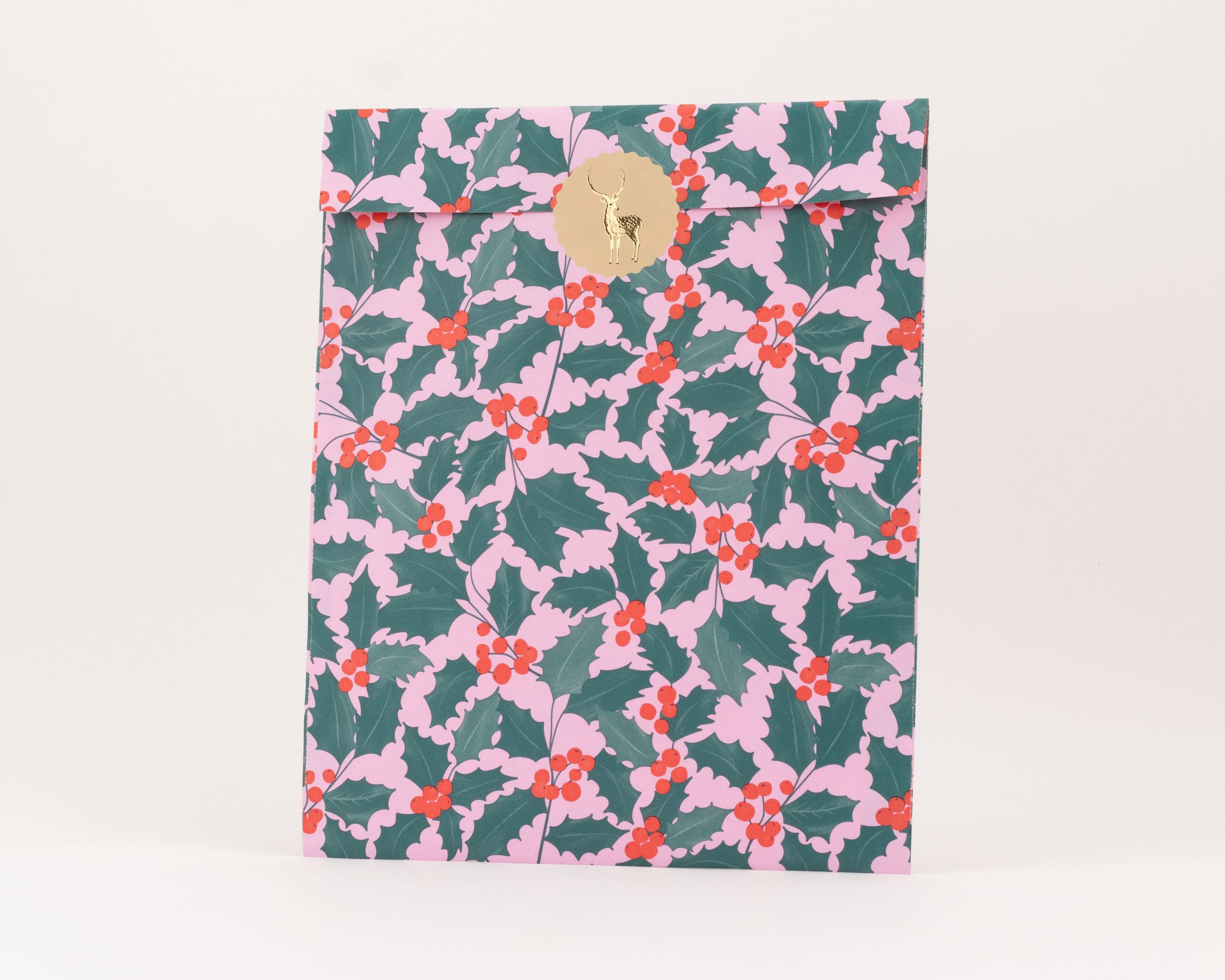 Flachbeutel mit rosa Hintergrund und grünem Ilex-Muster, verziert mit roten Beeren und einem goldenen Aufkleber mit Rentier-Motiv