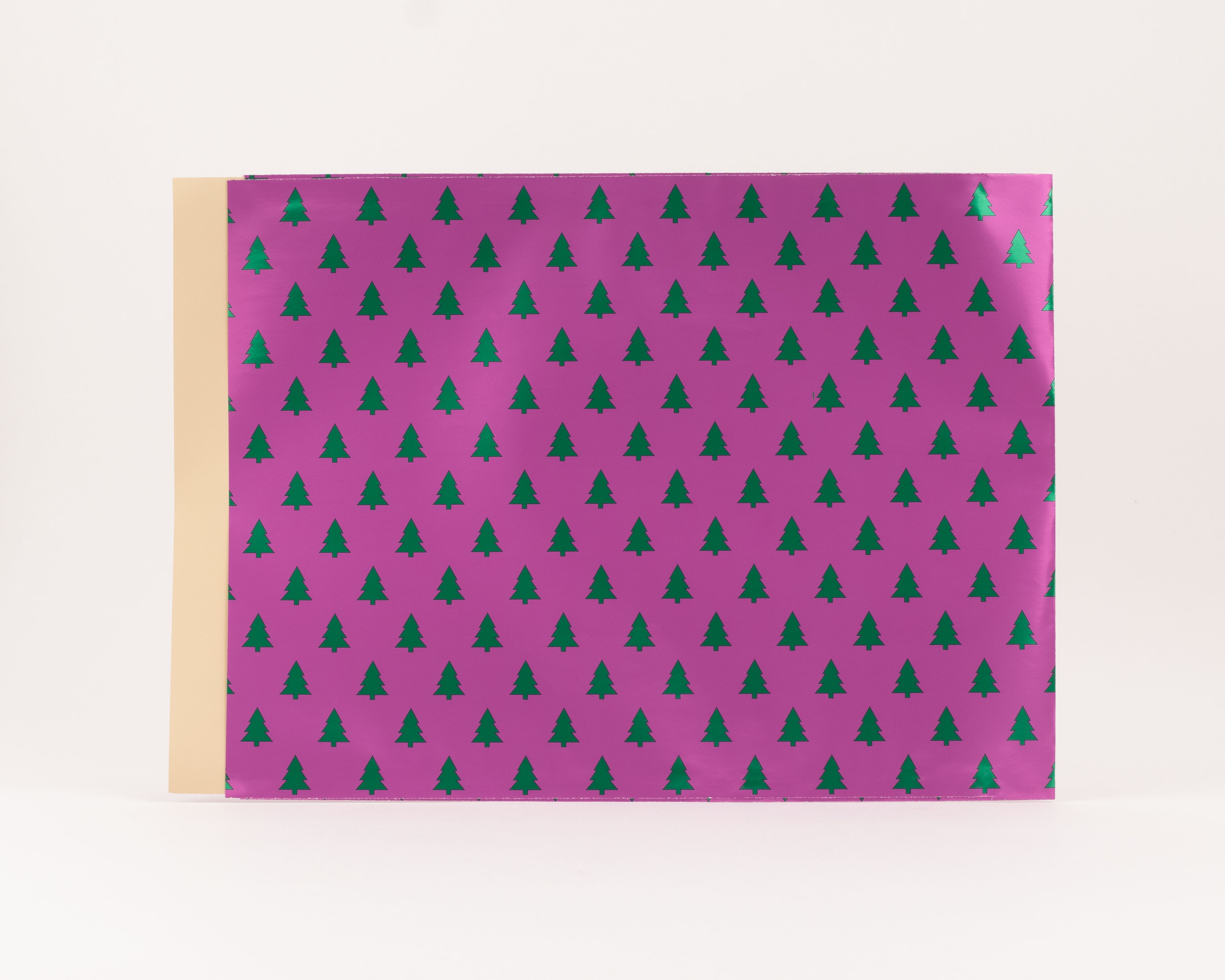 Flachbeutel mit einem pinken Hintergrund und einem wiederkehrenden Muster aus metallisch gruenen Tannenbaeumen, wobei die Innenseite beige ist