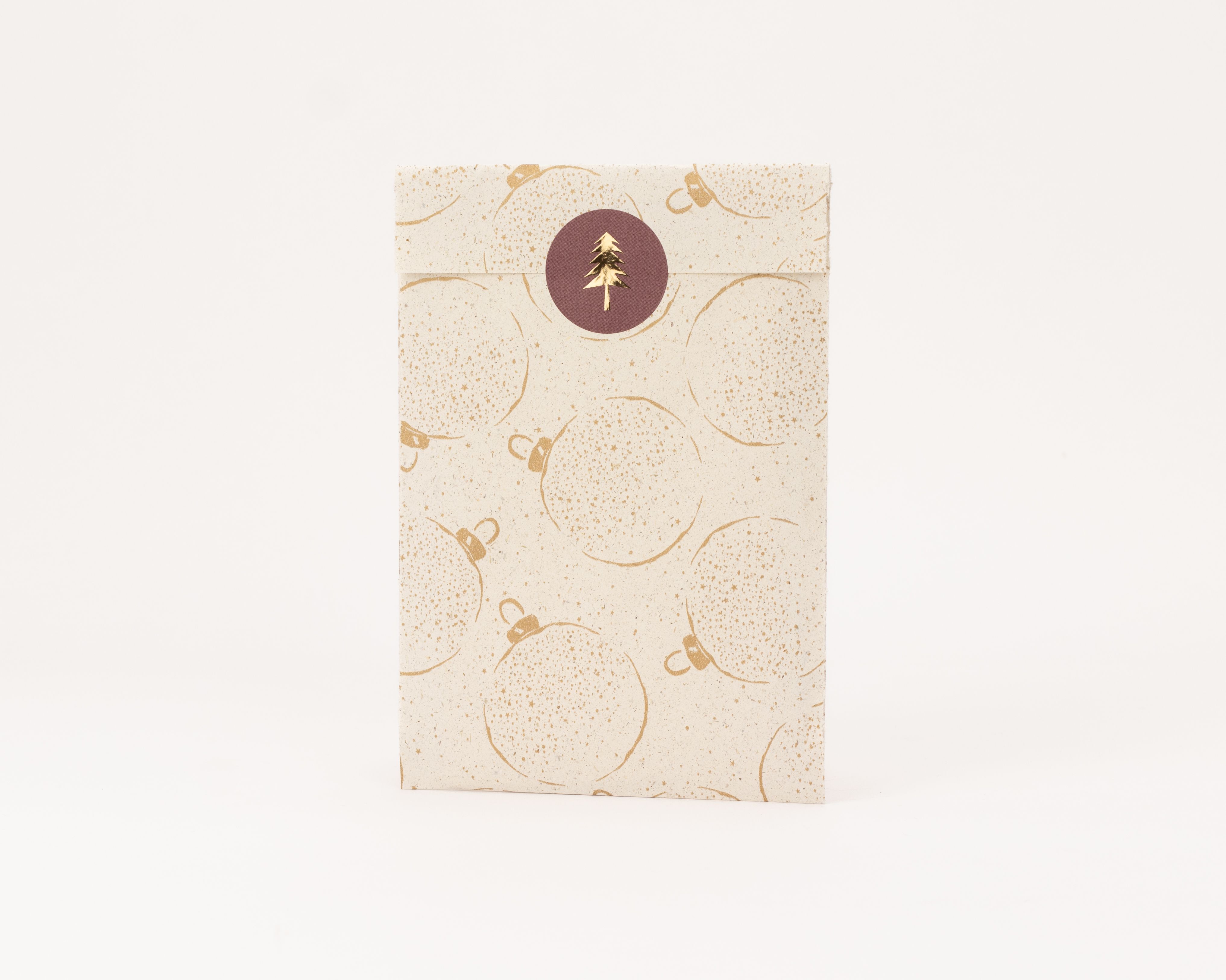 Flachbeutel aus Kraftpapier mit goldenem Weihnachtskugelmuster. Ein runder Aufkleber mit goldenem Weihnachtsbaum verschließt den Beutel