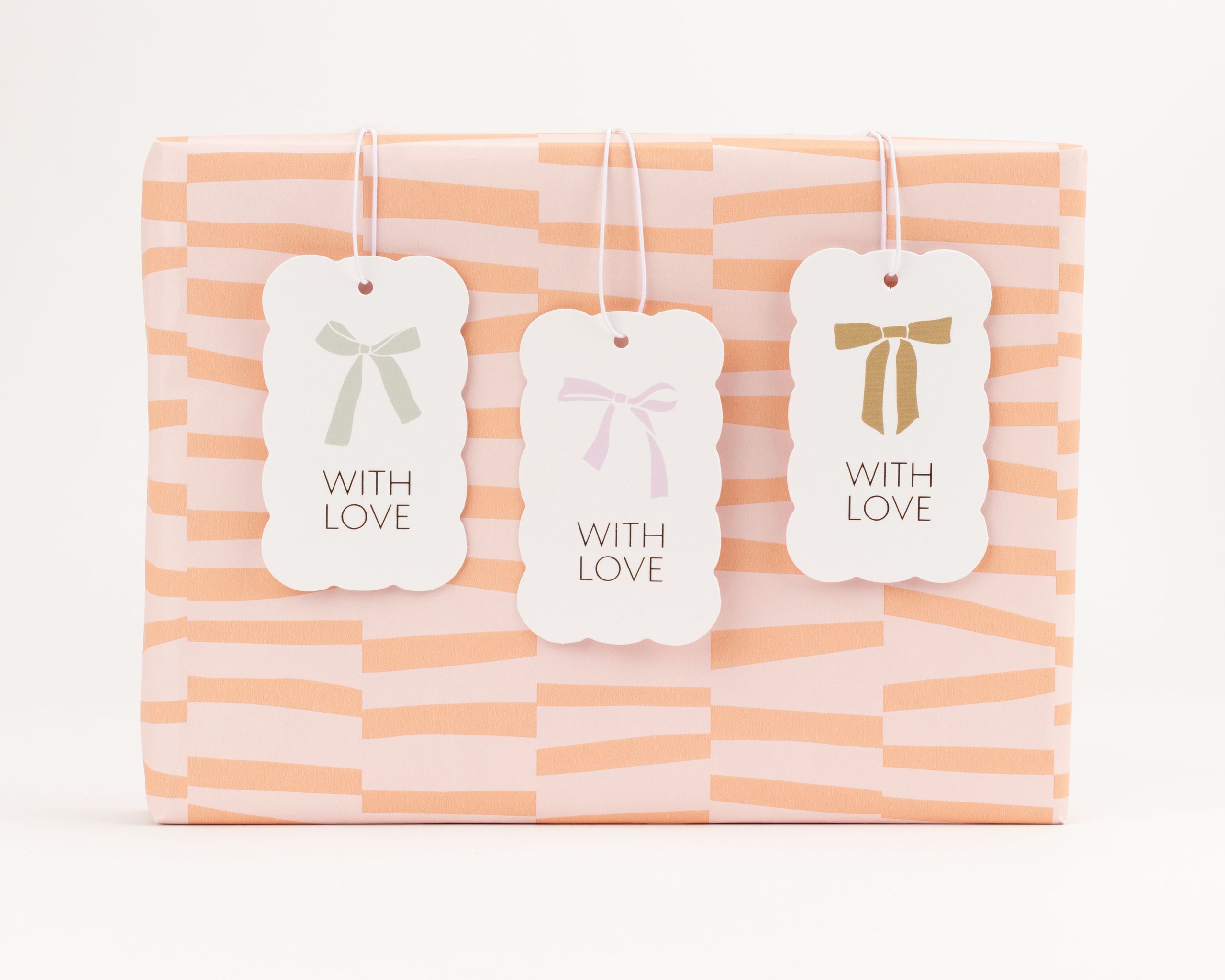 Geschenkanhänger-Set mit drei weißen Anhängern in gewellter Form, bedruckt mit Schleifenmotiven in Hellgrün, Hellrosa und Goldfarben