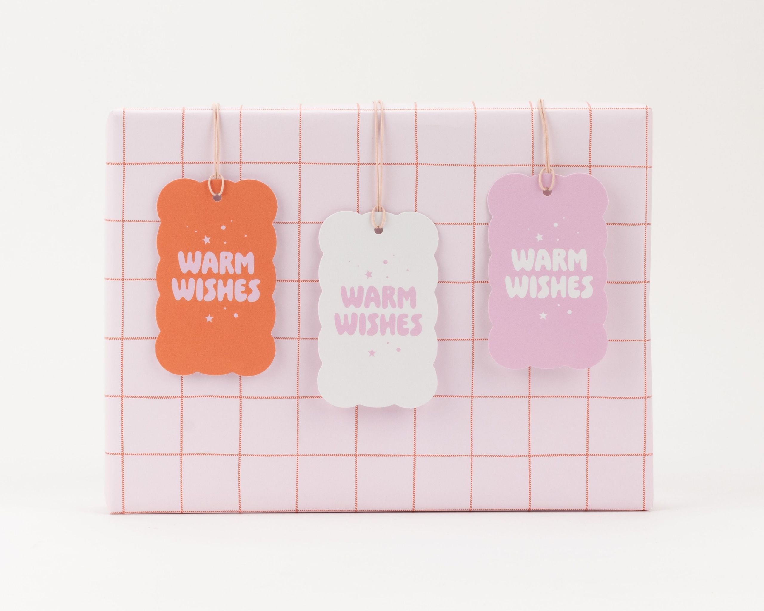 Geschenkanhänger-Set mit drei gewellten Anhängern in Orangerot, Weiß und Rosa mit 'Warm Wishes' Schriftzug und Sternen