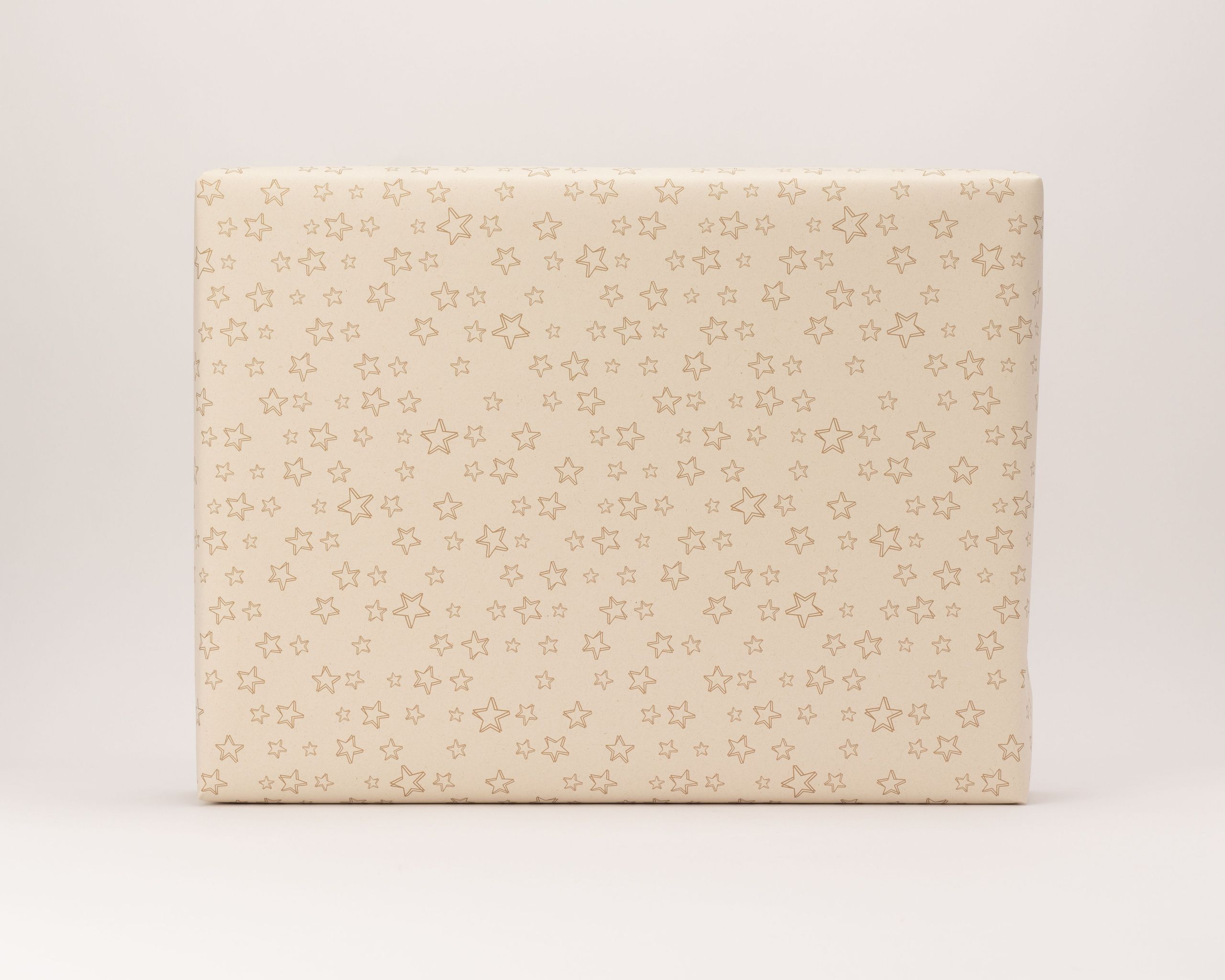 Geschenkpapier-Set, ein damit verpacktes Geschenk in hellem Kraftpapier. Das Papier zeigt ein Muster aus goldenen Umriss-Sternen
