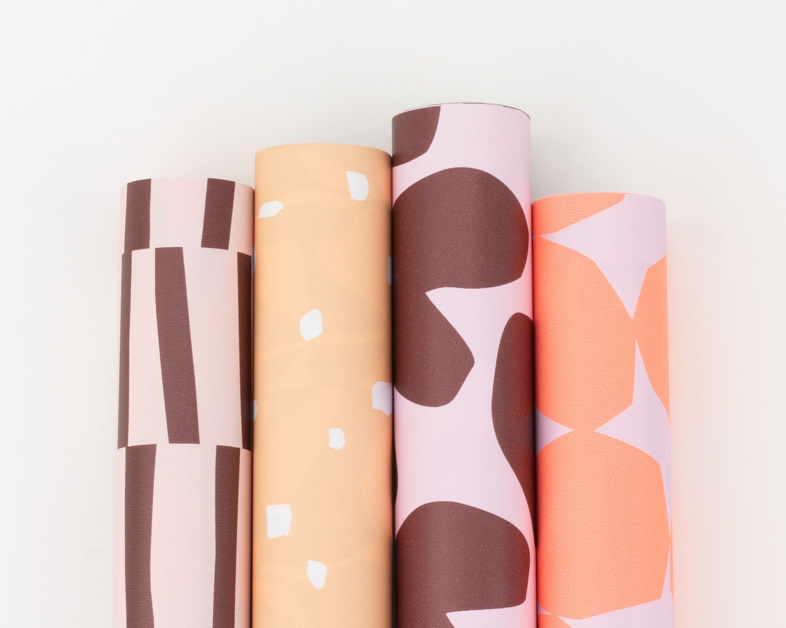 Geschenkpapier-Set mit vier Rollen in weinrot, rosa, peach und neonorangerot. Die Designs umfassen Streifen, Punkte und Herzmotive