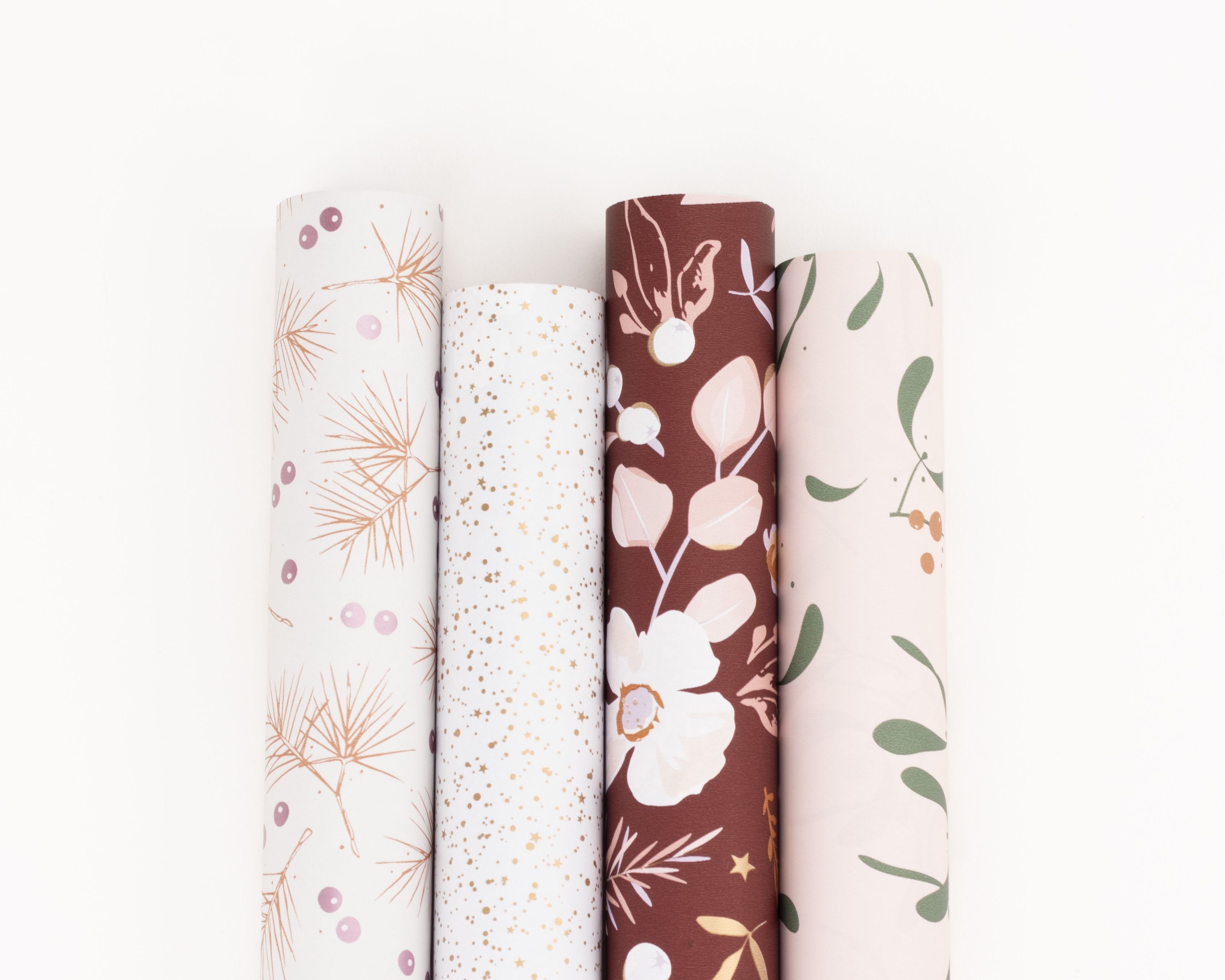 Geschenkpapier-Set mit vier Rollen in harmonischen Winterfarben, darunter cremeweiß, weiß, bordeauxrot und zartrosa mit floralen, sternen- und beerenförmigen Mustern