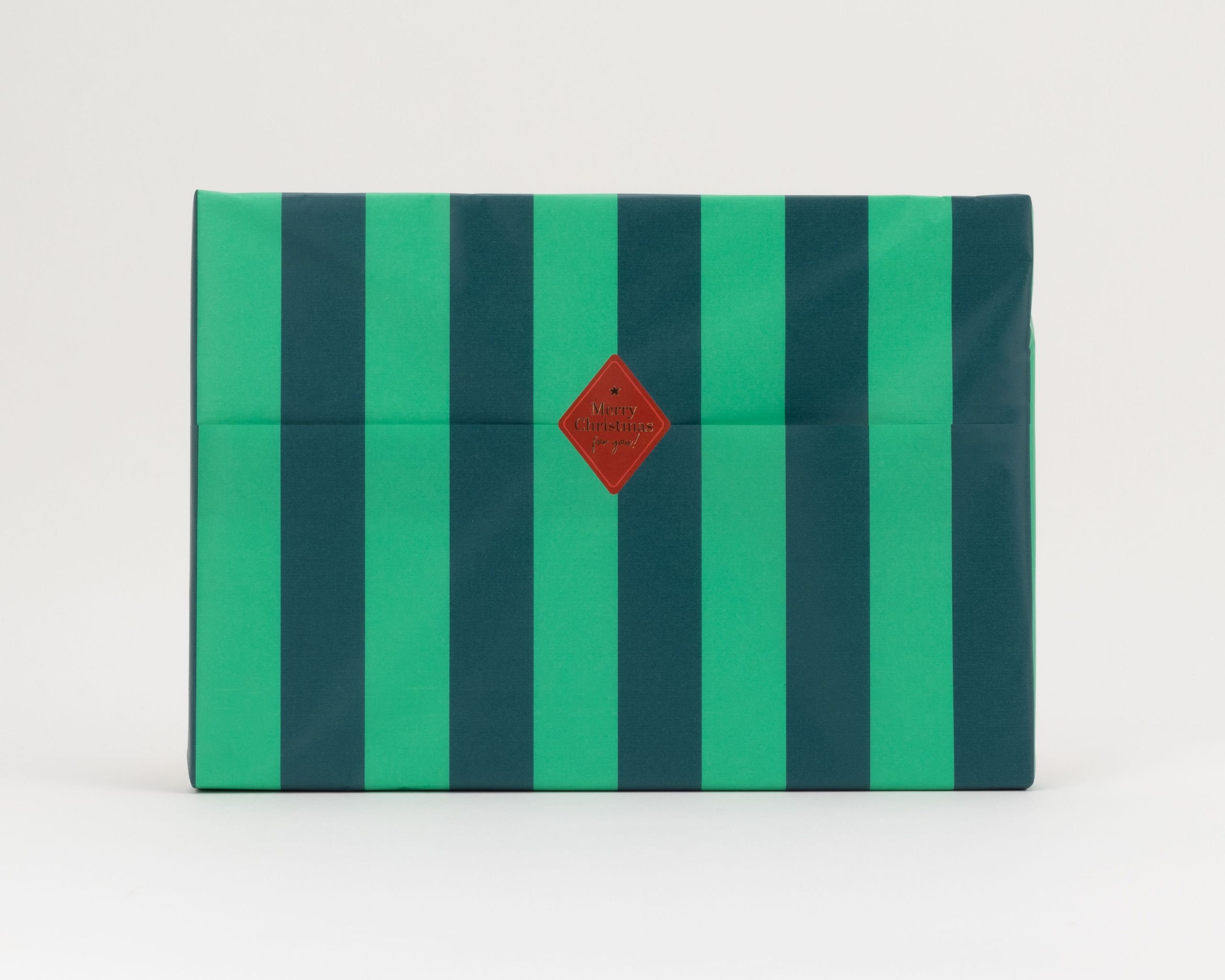 Seidenpapier mit breiten Blockstreifen in Grün und Dunkelgrün. Darauf ein roter, rautenförmiger Aufkleber mit goldener Schrift