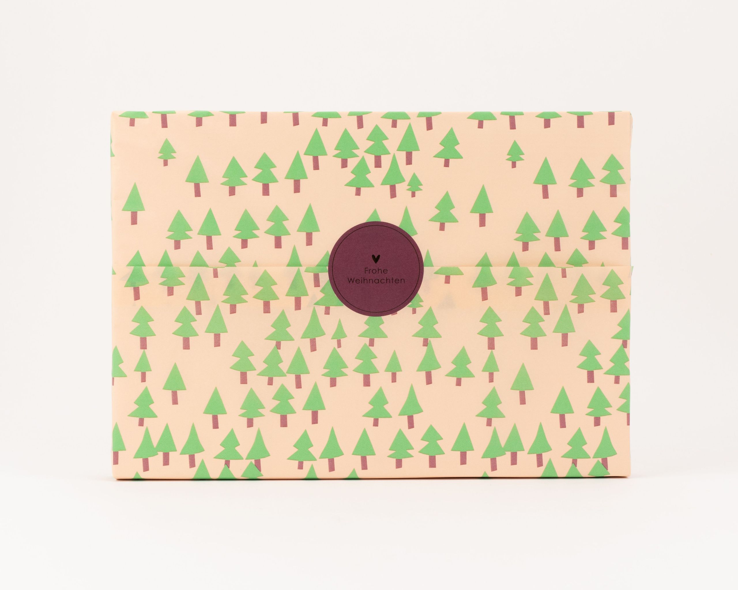 Seidenpapier mit hellbeigem Hintergrund und gruenen Tannenbaummustern. Ein dunkelroter runder Aufkleber zeigt Frohe Weihnachten