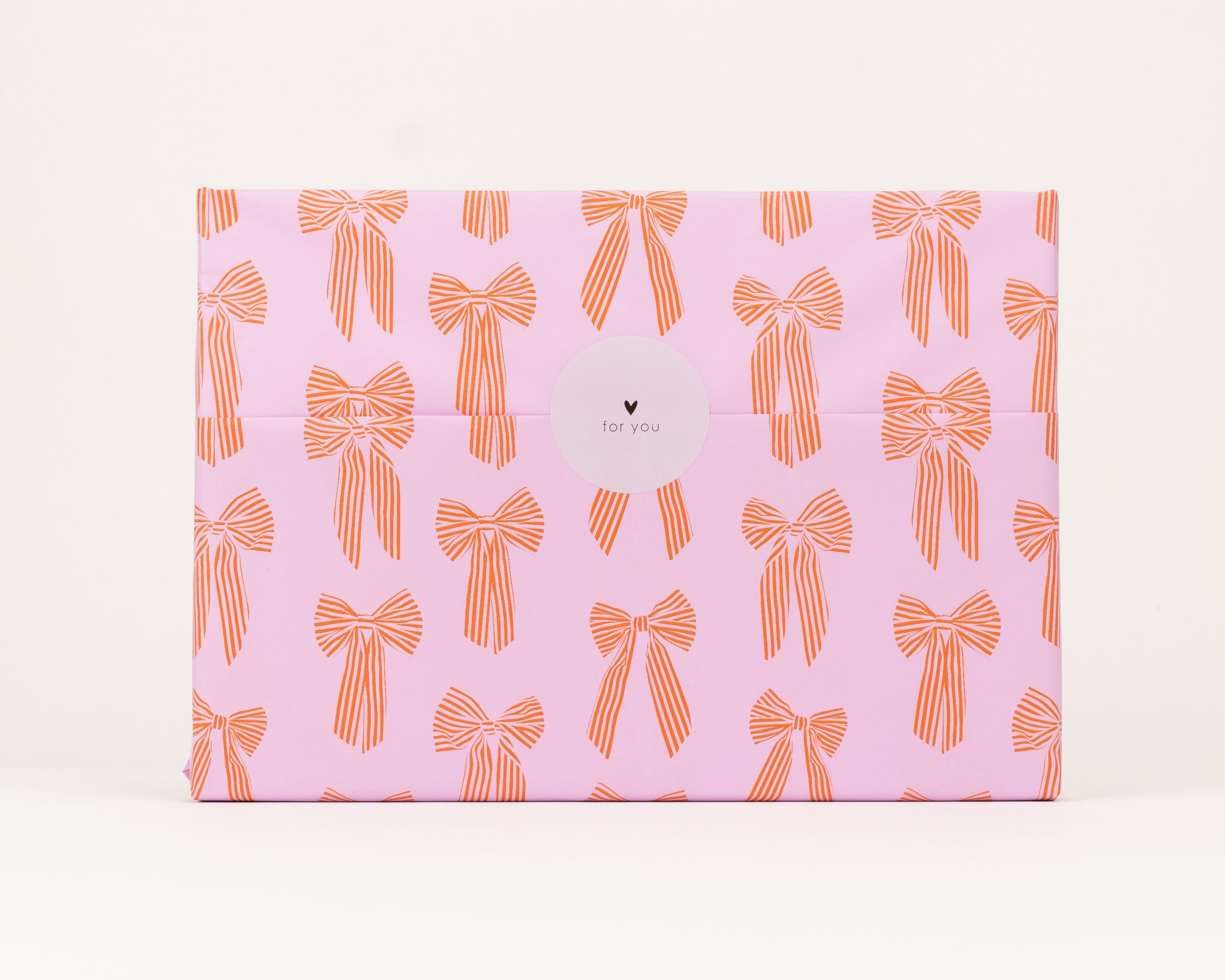 Seidenpapier in Pink mit roten Schleifen als Muster. Darauf ein weisser runder Aufkleber mit schwarzem Herz und dem Text for you