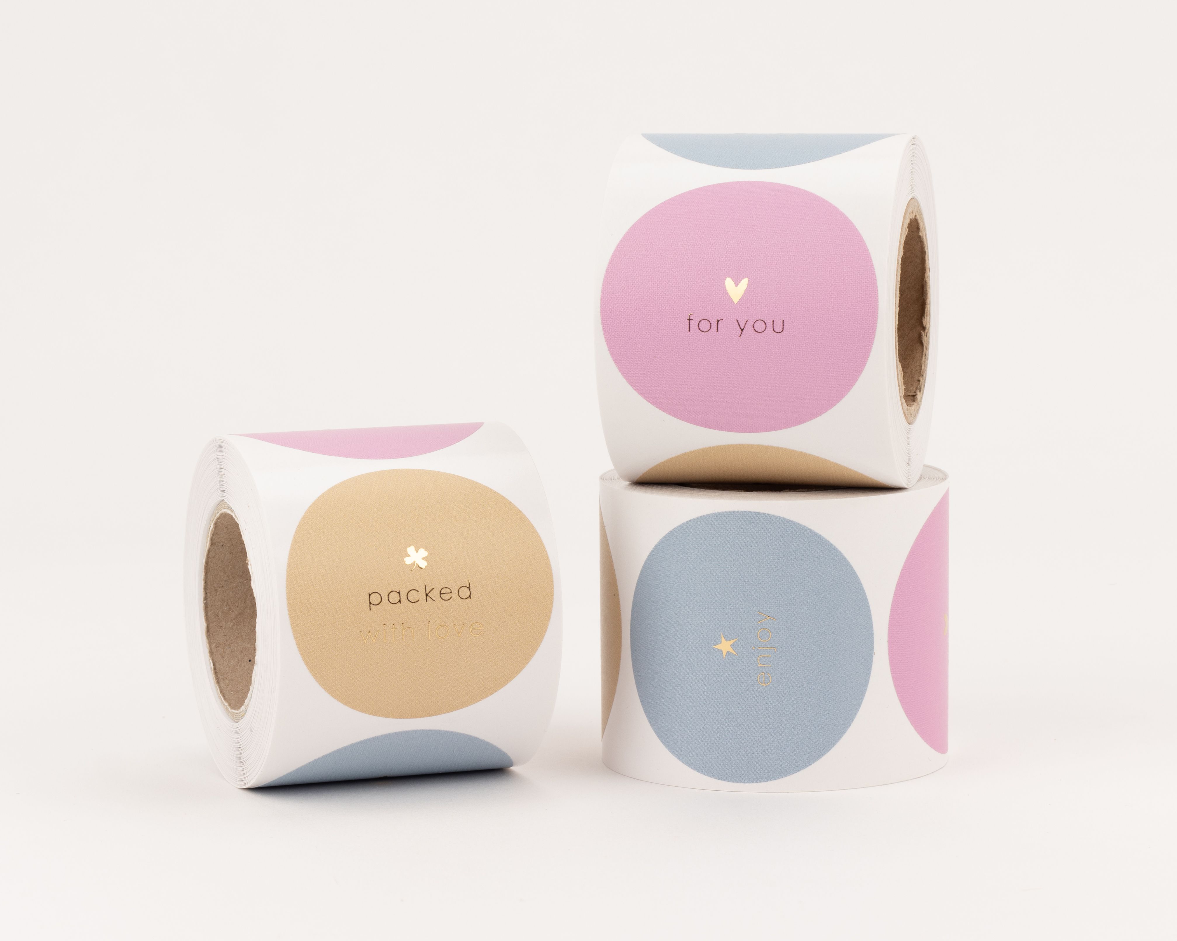 Aufkleber mit drei verschiedenen runden Designs in Pink, Beige und Blau, verziert mit goldfarbenen Schriftzügen und Motiven