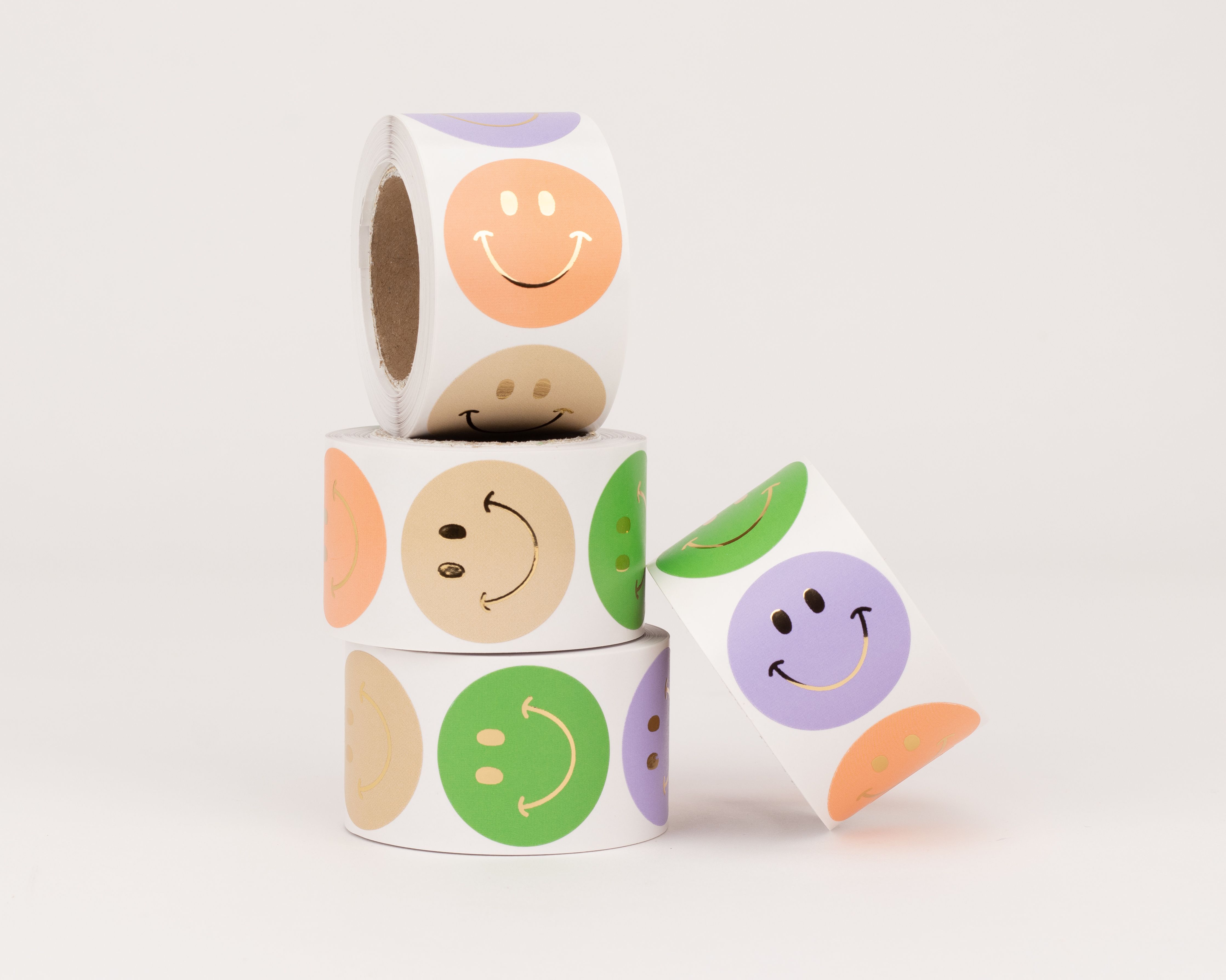 Aufkleber mit verschiedenen Smiley-Designs in Beige, Orange, Grün und Flieder, alle mit Gold-Effekt