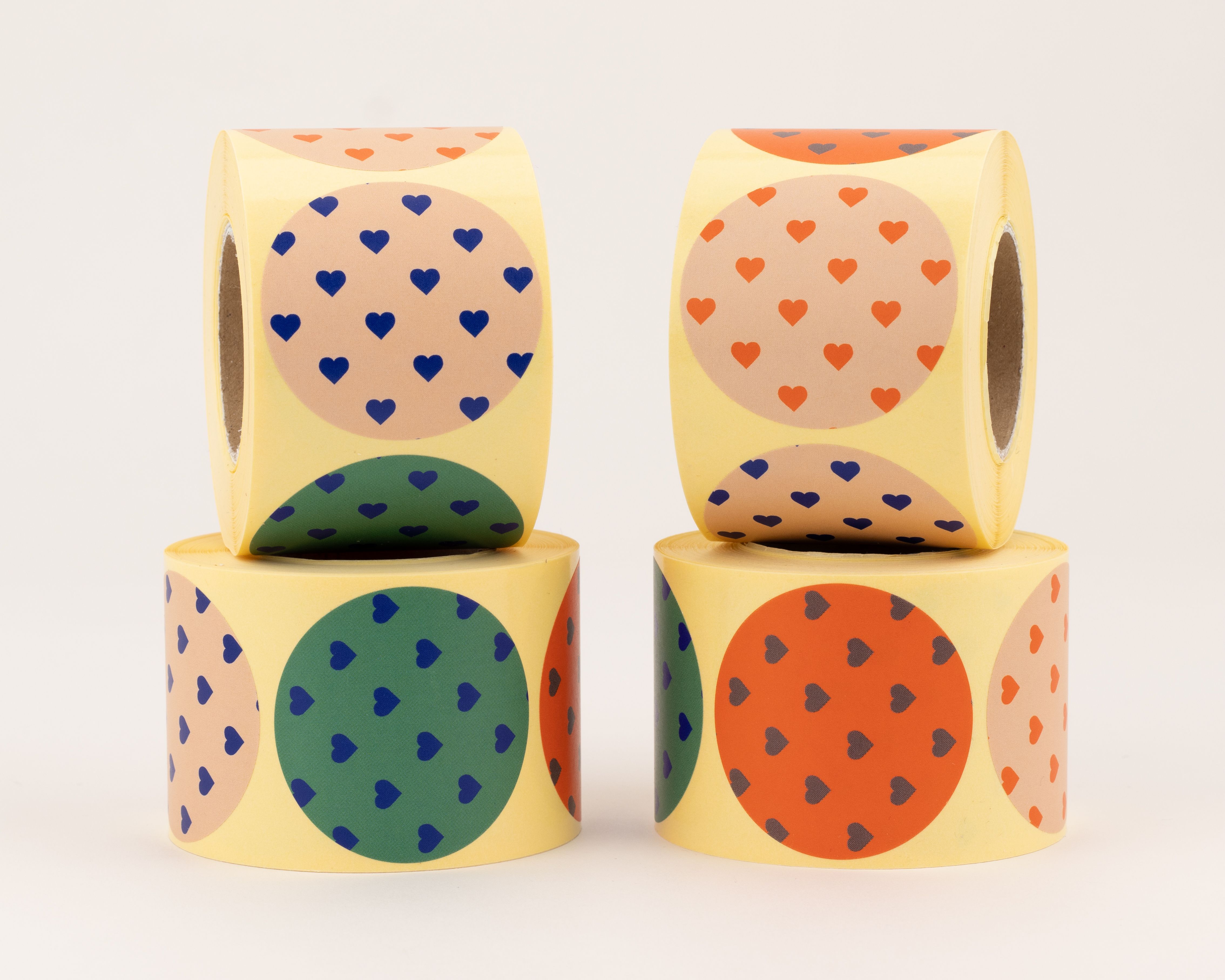 Aufkleber zeigen vier verschiedene runde Herzmotive: blaue auf Beige, orange auf Beige, blaue auf Grün und dunkle Herzen auf Orange