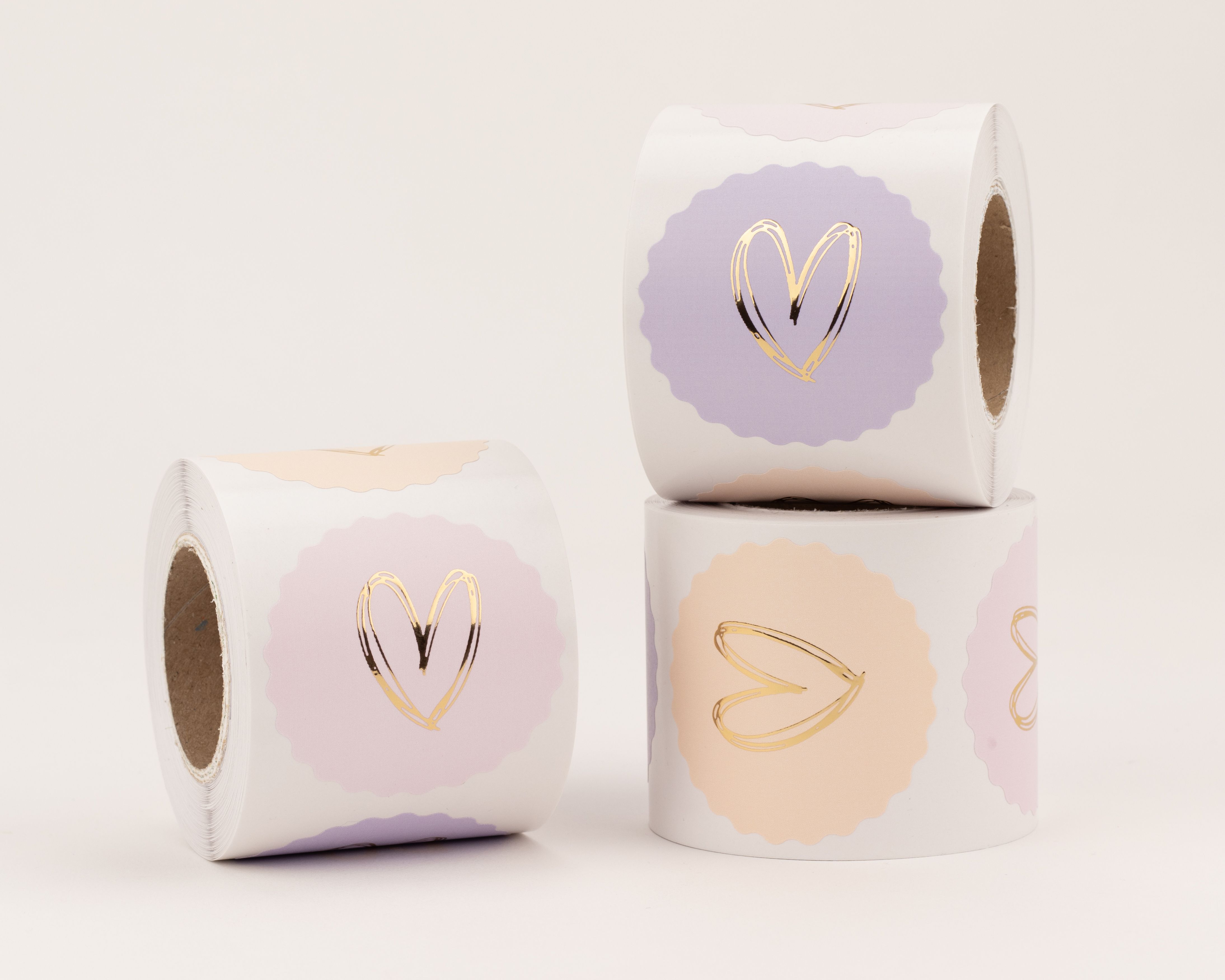 Aufkleber mit drei verschiedenen Herzmotiven in Gold-Effekt auf rosa, hellfliederfarbenem und pfirsichfarbenem Hintergrund