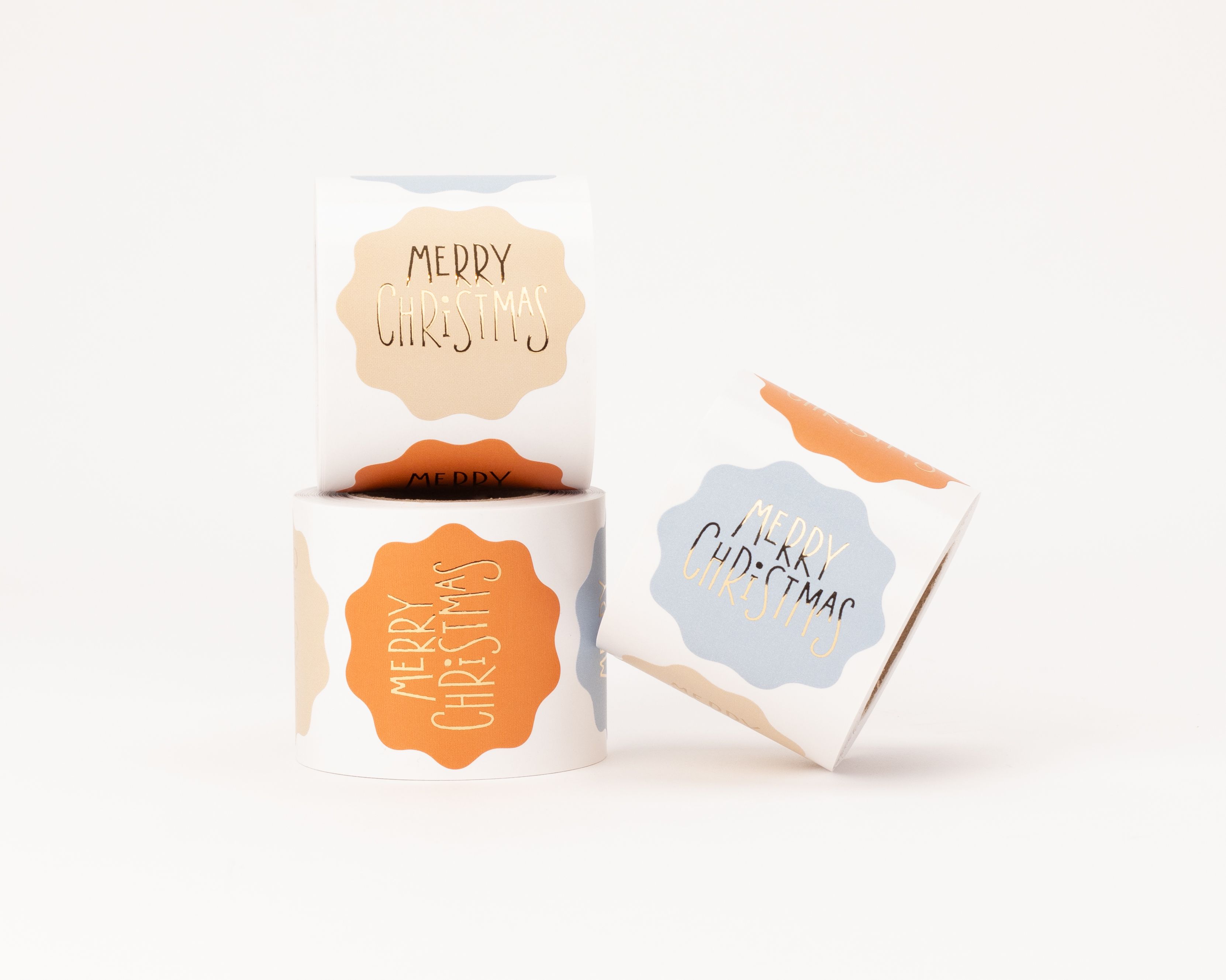 Aufkleber in verschiedenen Designs mit den Farben Beige, Orange und Blau. Sie zeigen den goldfarbenen Merry Christmas Schriftzug in gewellter Form
