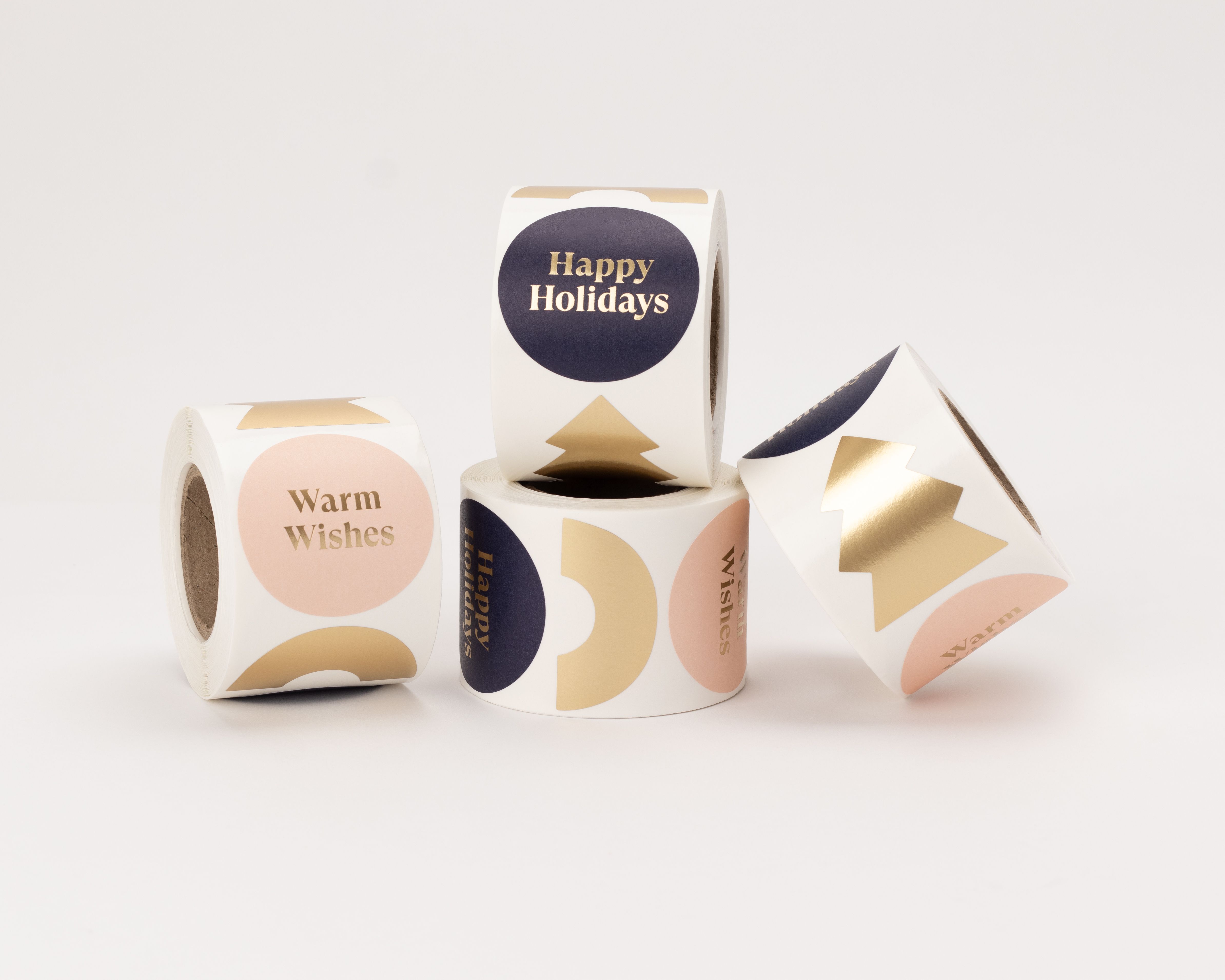 Aufkleber mit vier verschiedenen Designs in Blau, Rosa und Gold. Sie zeigen goldene Schriftzüge wie 'Warm Wishes' und 'Happy Holidays' sowie goldene Bäume