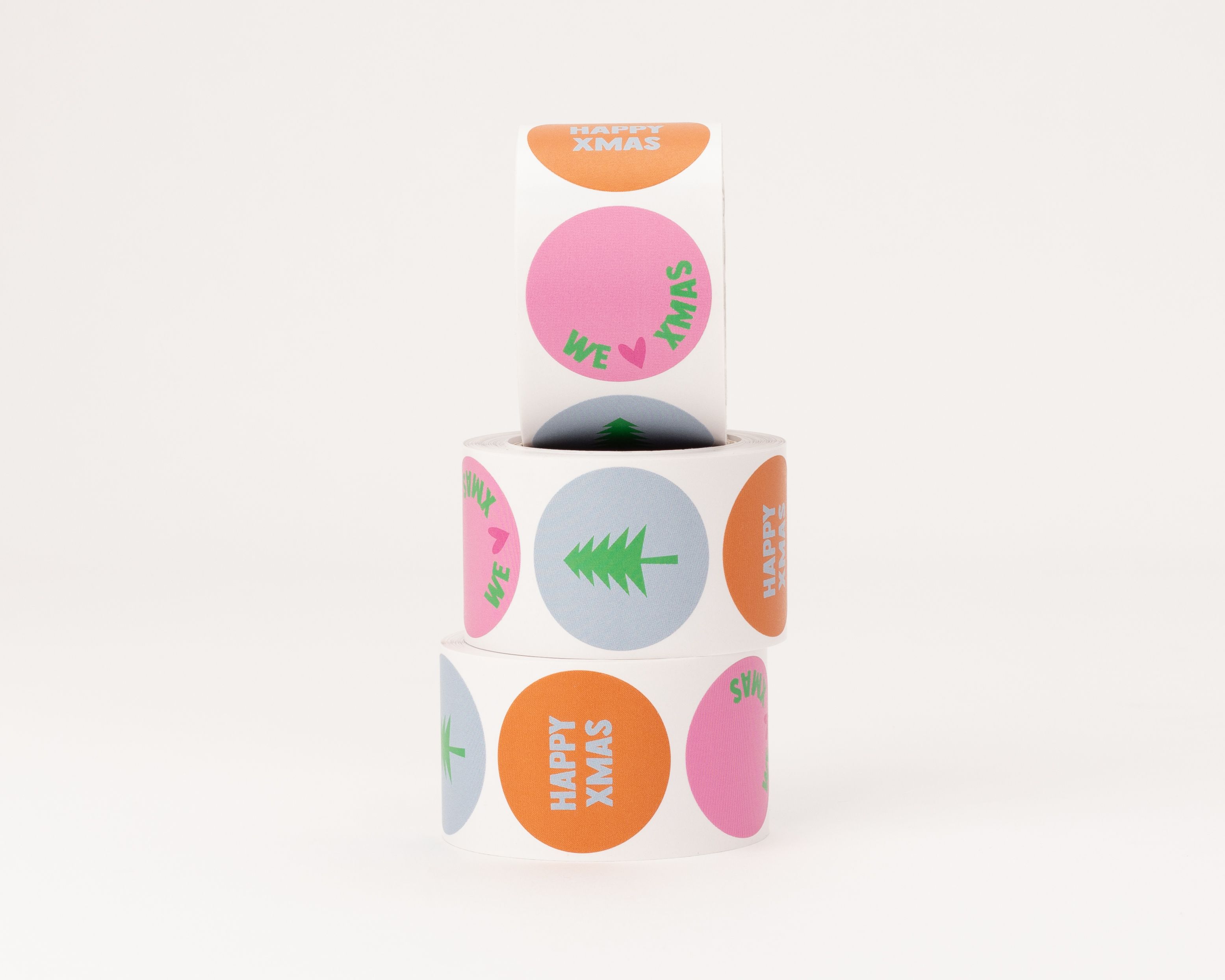 Weihnachts-Aufkleber mit drei verschiedenen runden Designs. Sticker in Pink, Blau und Zimt mit grünen Schriftzügen und einem Tannenbaum