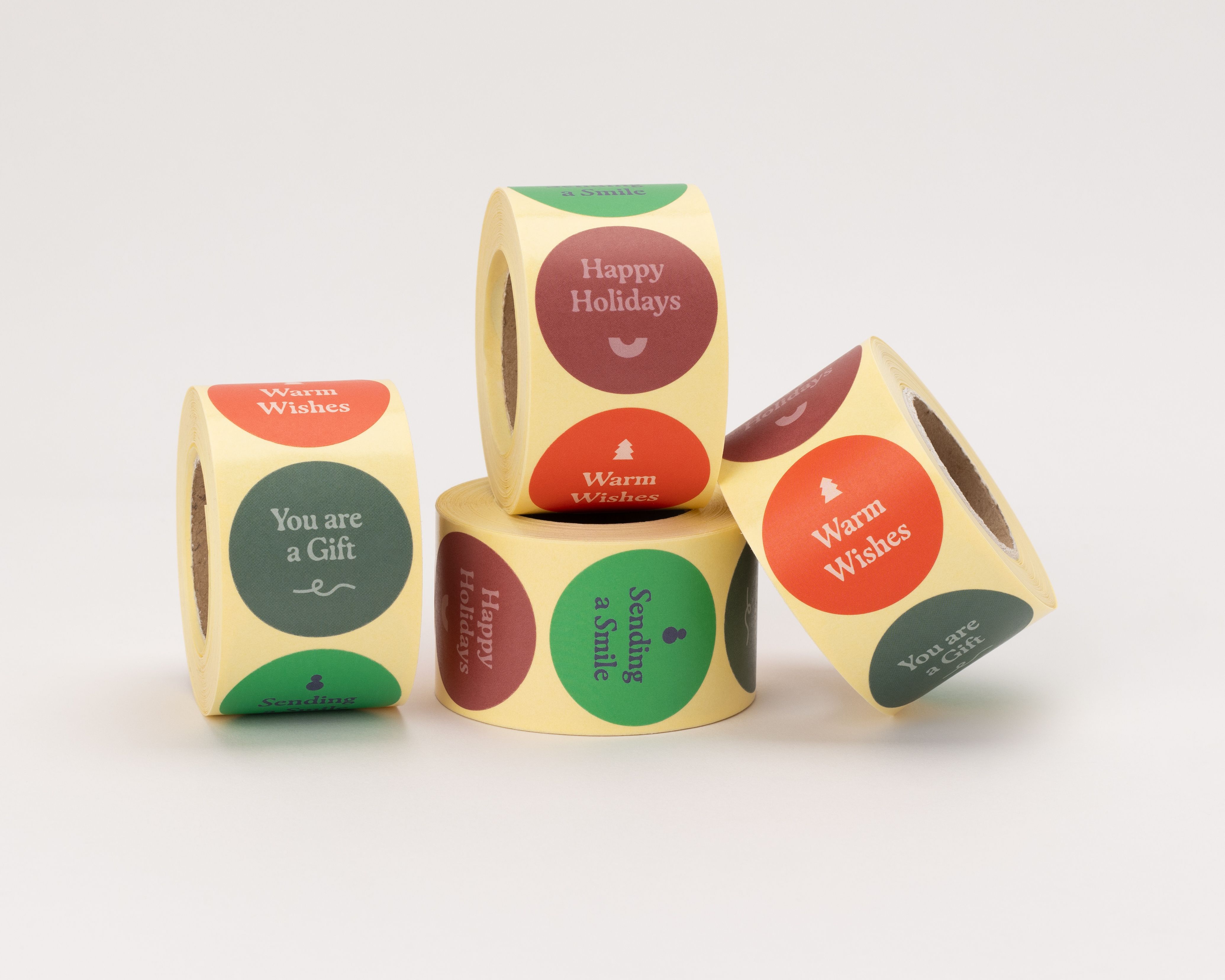 Aufkleber mit vier verschiedenen weihnachtlichen Designs in Grün, Rot, Burgunderrot und Blau, mit Sprüchen wie 'Warm Wishes' und 'Happy Holidays'