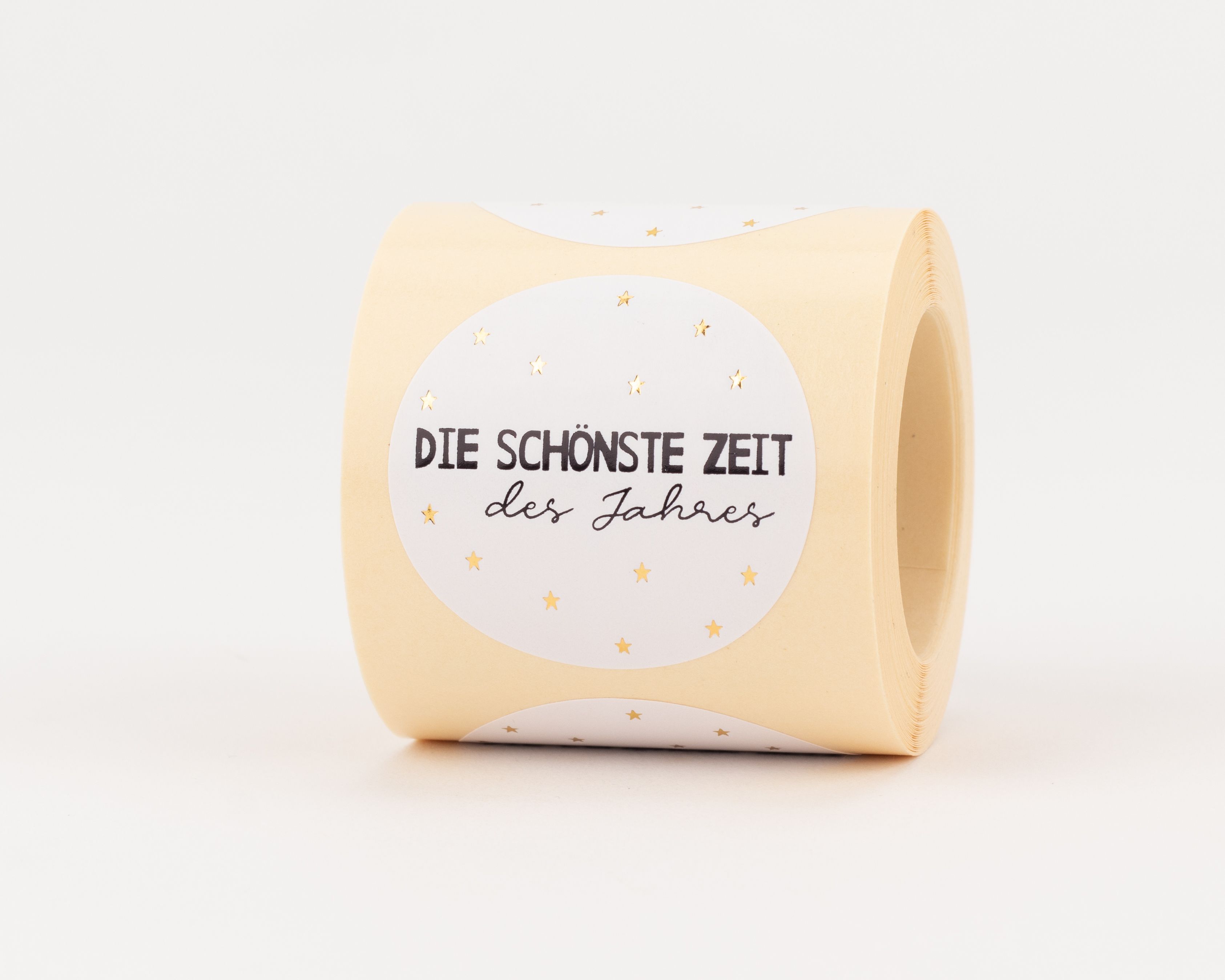 Aufkleber zeigen ein beiges Design mit weißem Oval, schwarzem Text 'DIE SCHÖNSTE ZEIT des Jahres' und goldglänzenden Sternen