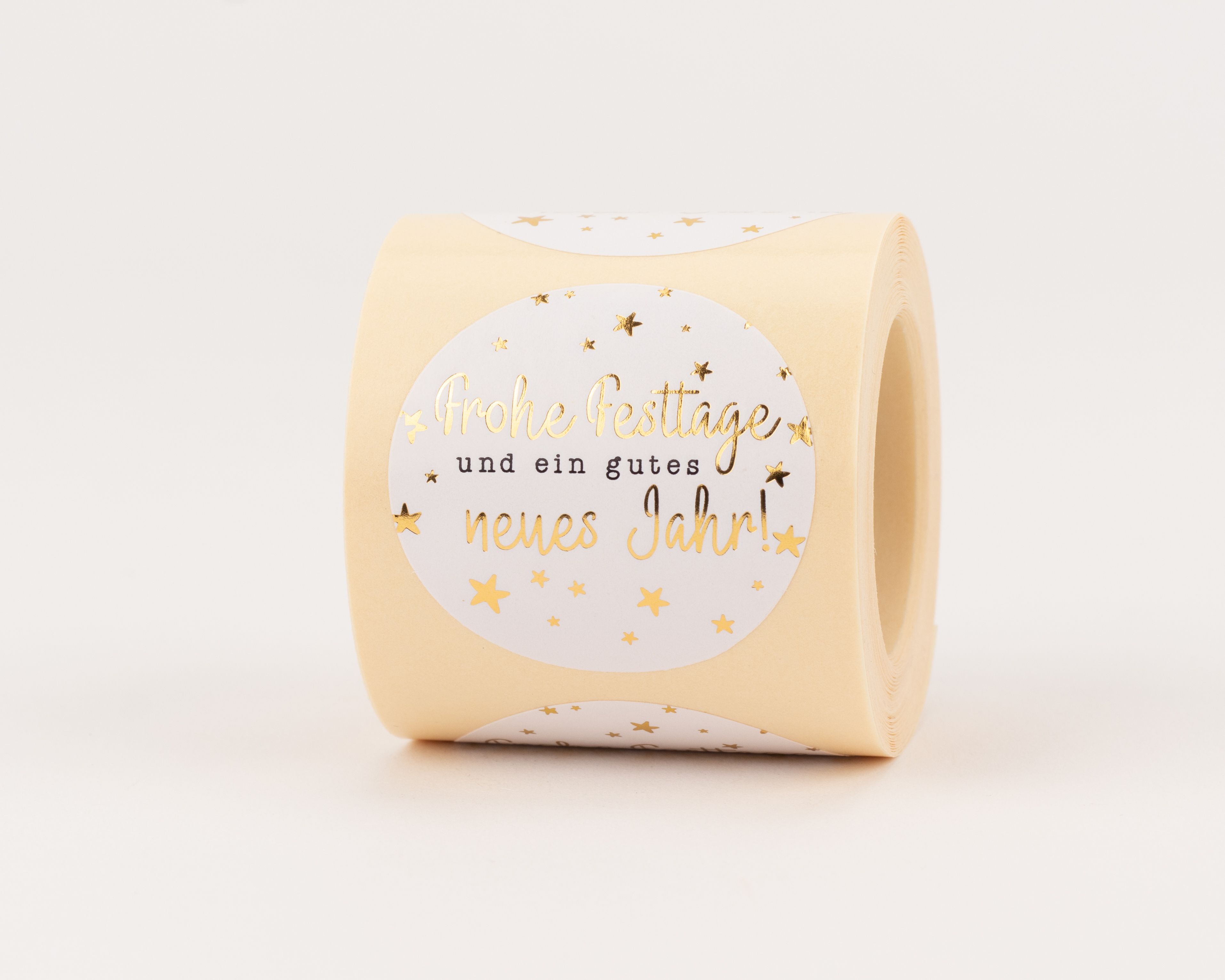 Aufkleber mit goldener Schrift 'Frohe Festtage und ein gutes neues Jahr!' und goldenen Sternen auf hellbeigem Grund