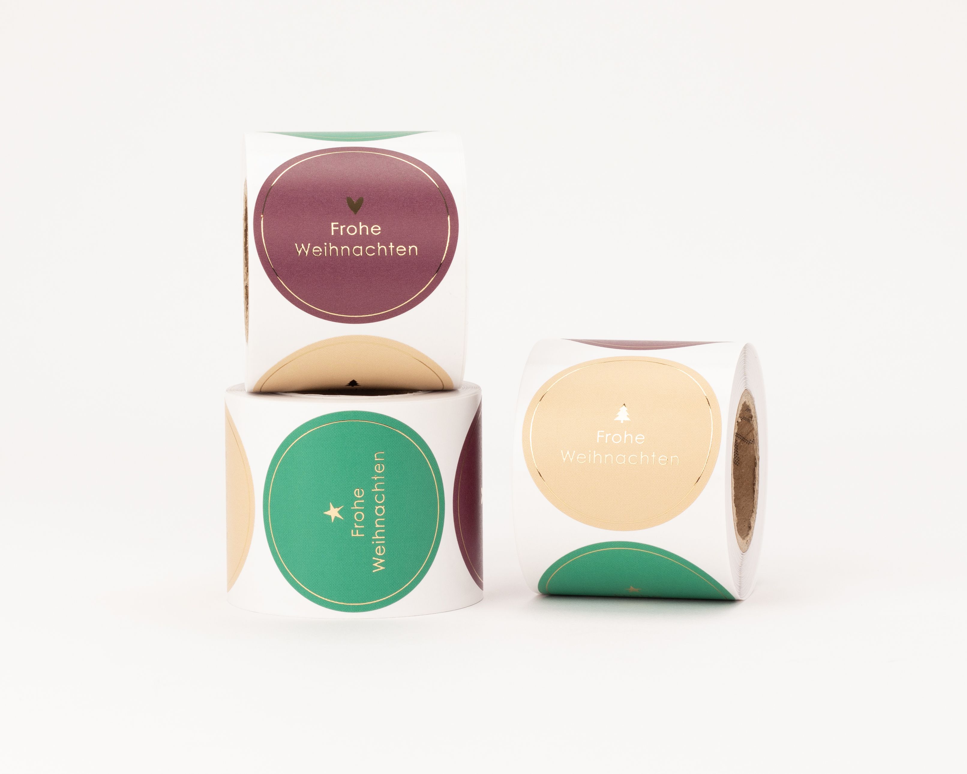 Aufkleber mit 'Frohe Weihnachten' Schriftzug. Runde Sticker in Beige, Grün, Burgunderrot zeigen goldene Herz-, Stern- und Tannenmotive