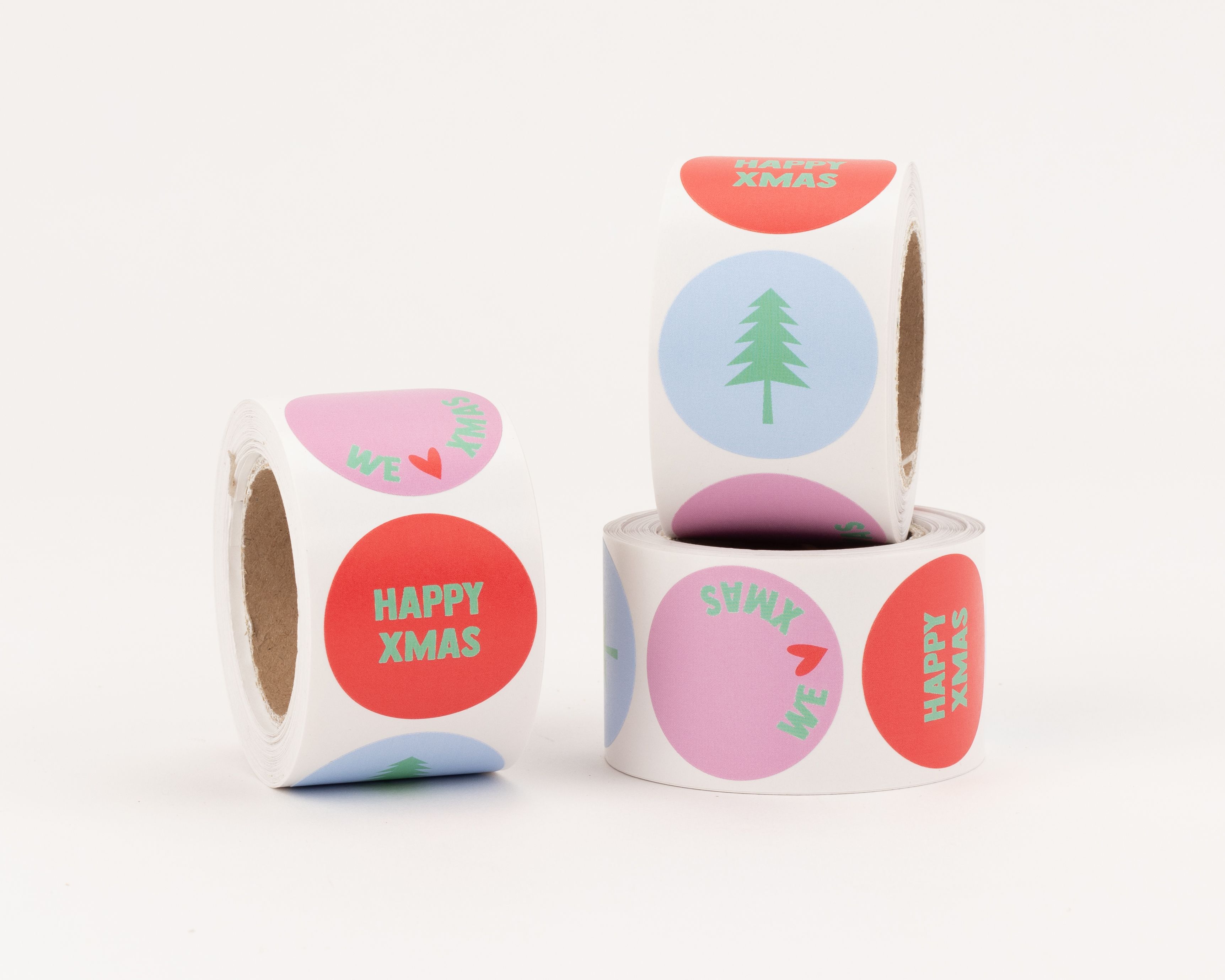 Aufkleber mit drei verschiedenen Weihnachtsmotiven. Rote Sticker mit 'Happy Xmas' Schriftzug, hellblaue mit Tannenbaum und pinke mit 'We ♥' Text
