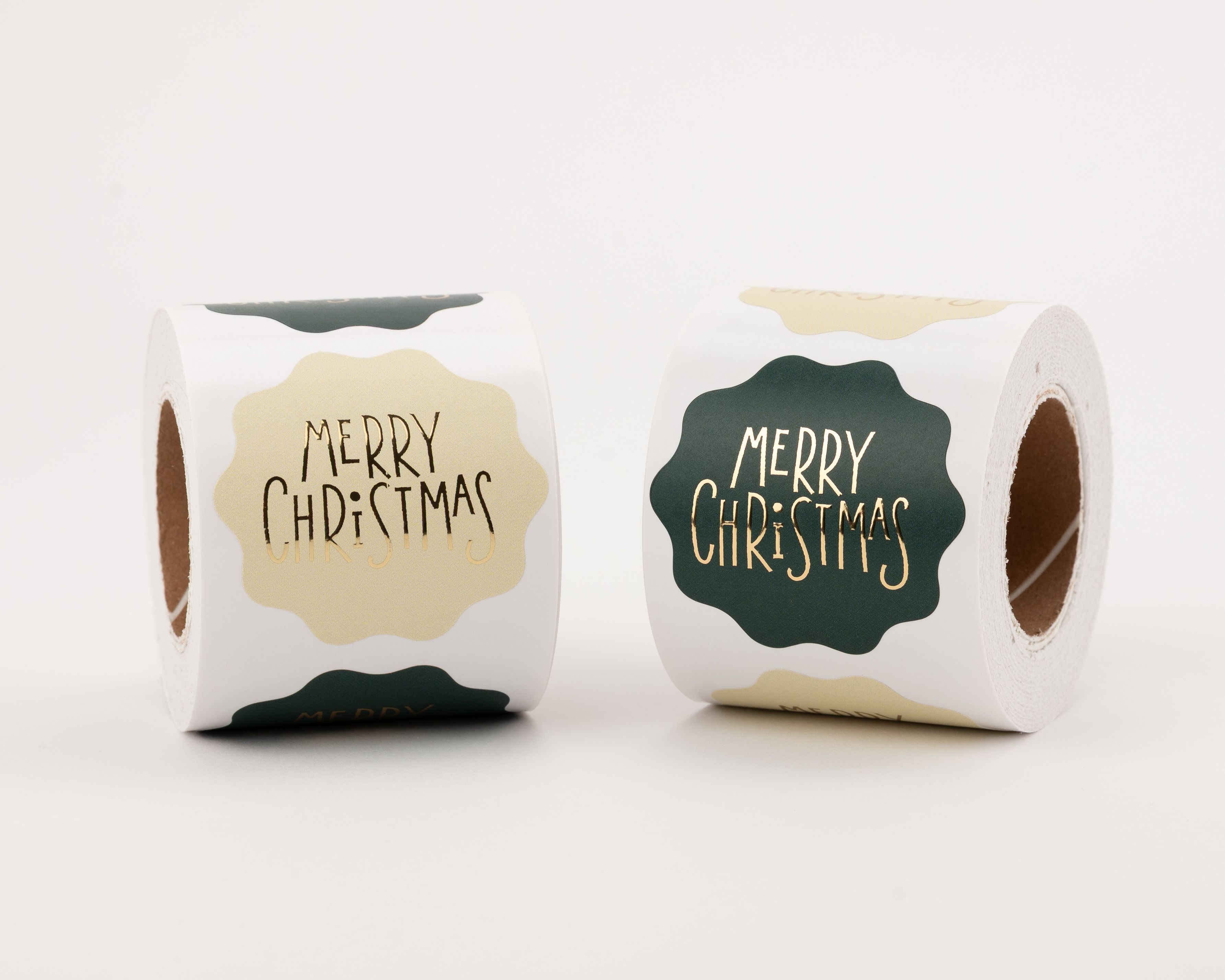 Runde Aufkleber mit wellenförmigem Rand und goldener Merry Christmas Aufschrift. Die Designs sind elfenbeinfarben oder dunkelgrün