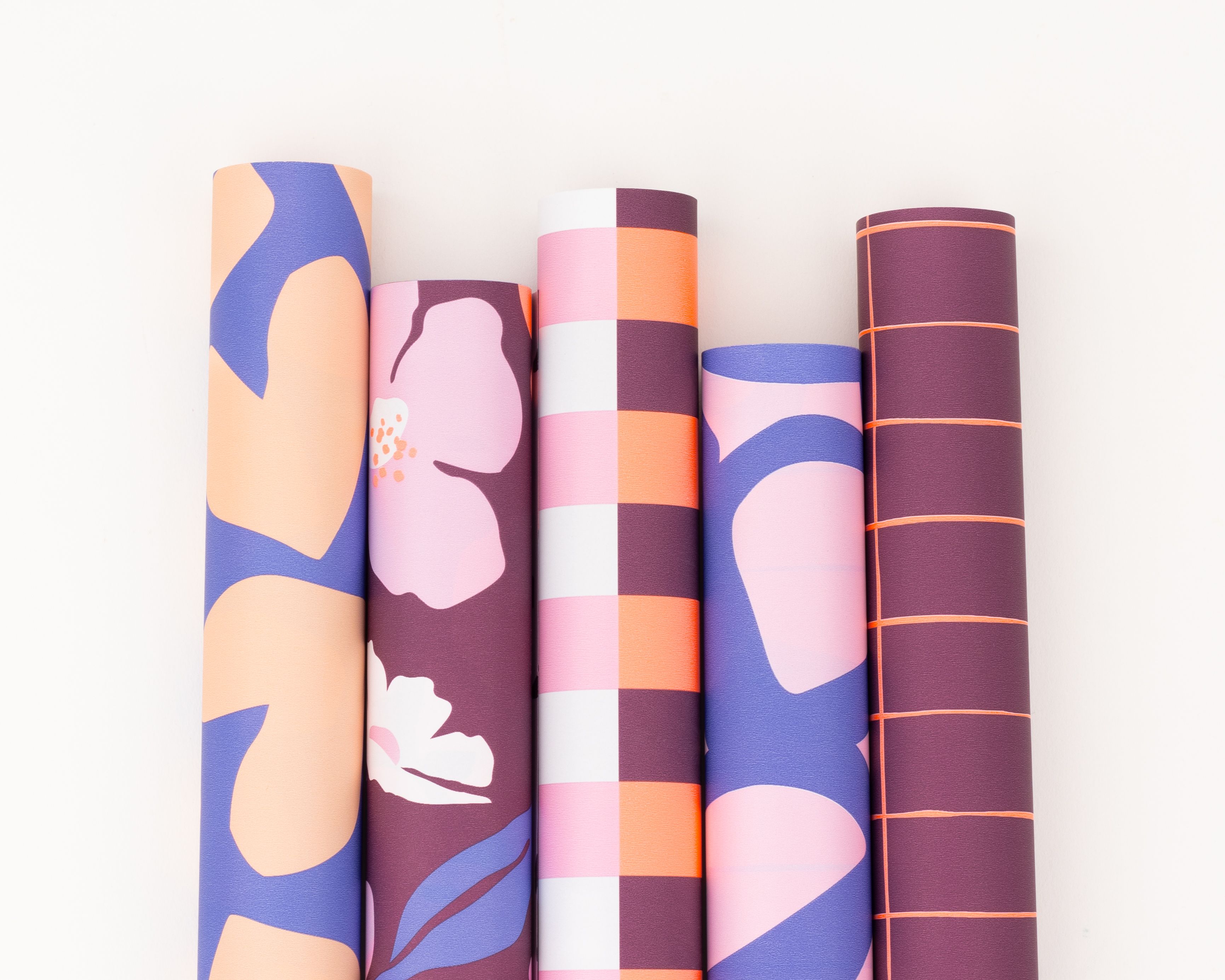 Geschenkpapier-Set mit fünf bunten Rollen in Aubergine, Blau, Pink und Orange. Die Rollen zeigen abstrakte und grafische Muster