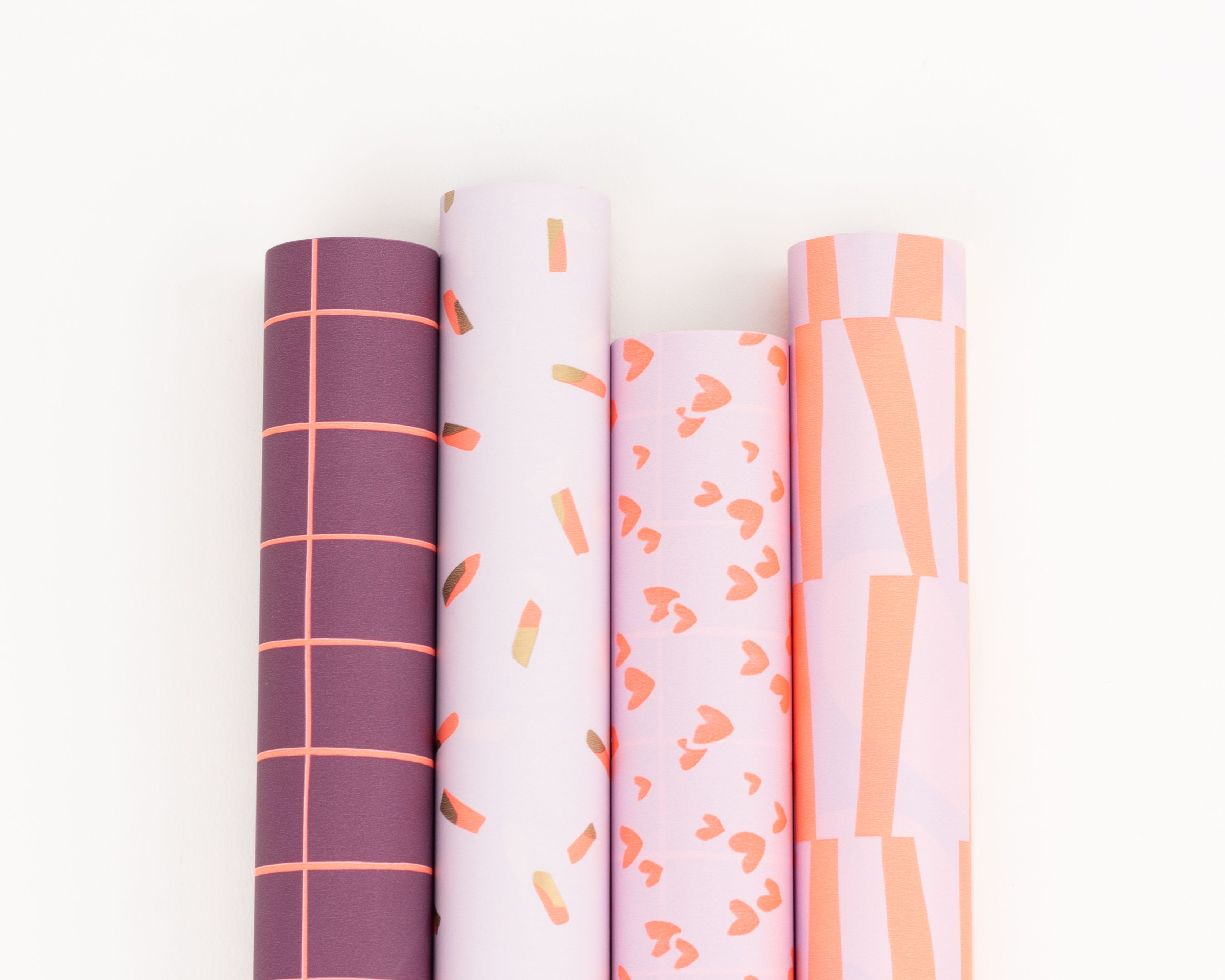 Geschenkpapier-Set mit vier Rollen in Lila-, Rosa- und Orangetönen. Die Designs umfassen Gitter, Streusel, Herzen und breite Striche
