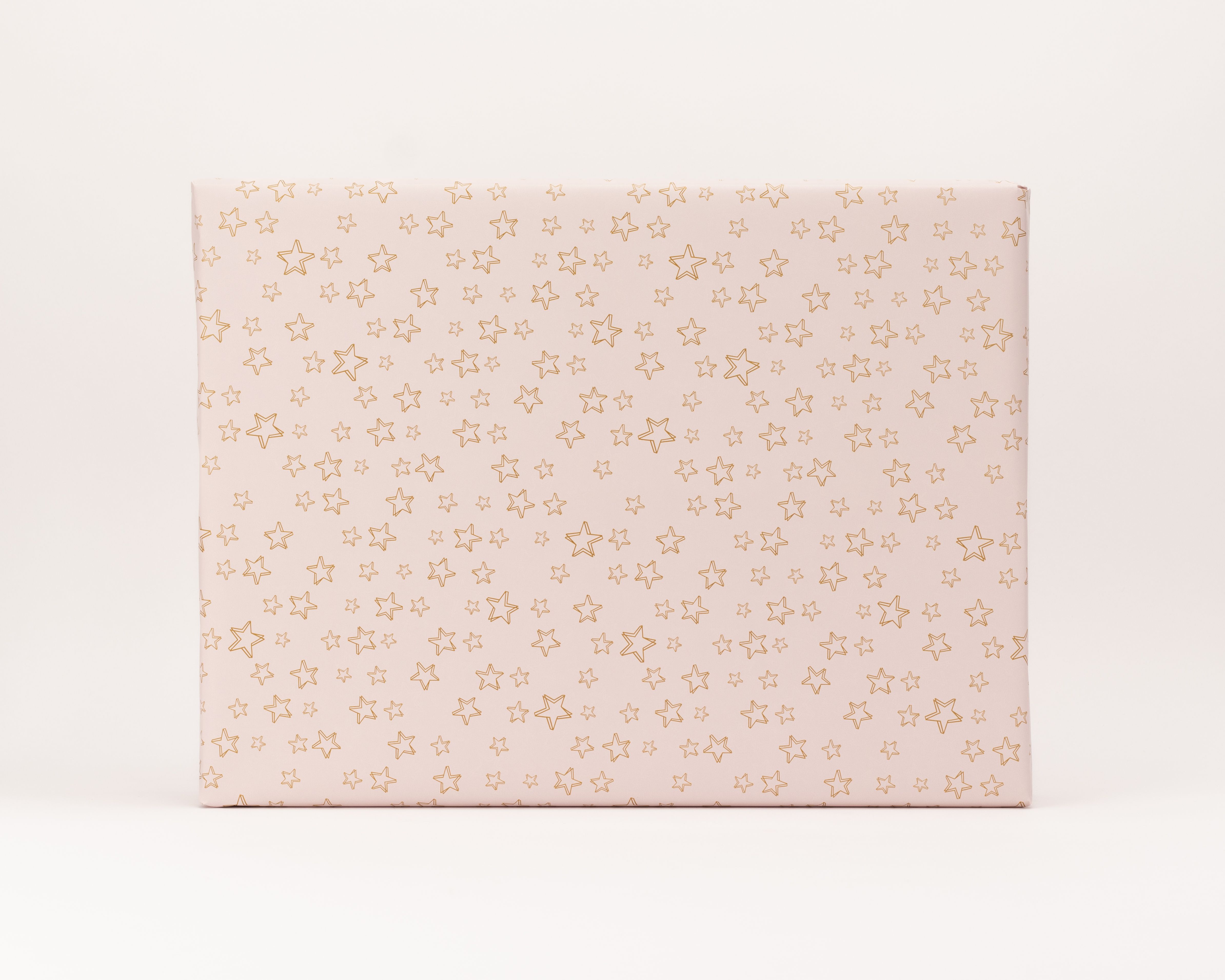 Geschenkpapier-Set, eine Geschenkbox ist in zartrosa Papier mit glänzenden, roségoldenen Sternumrissen verpackt