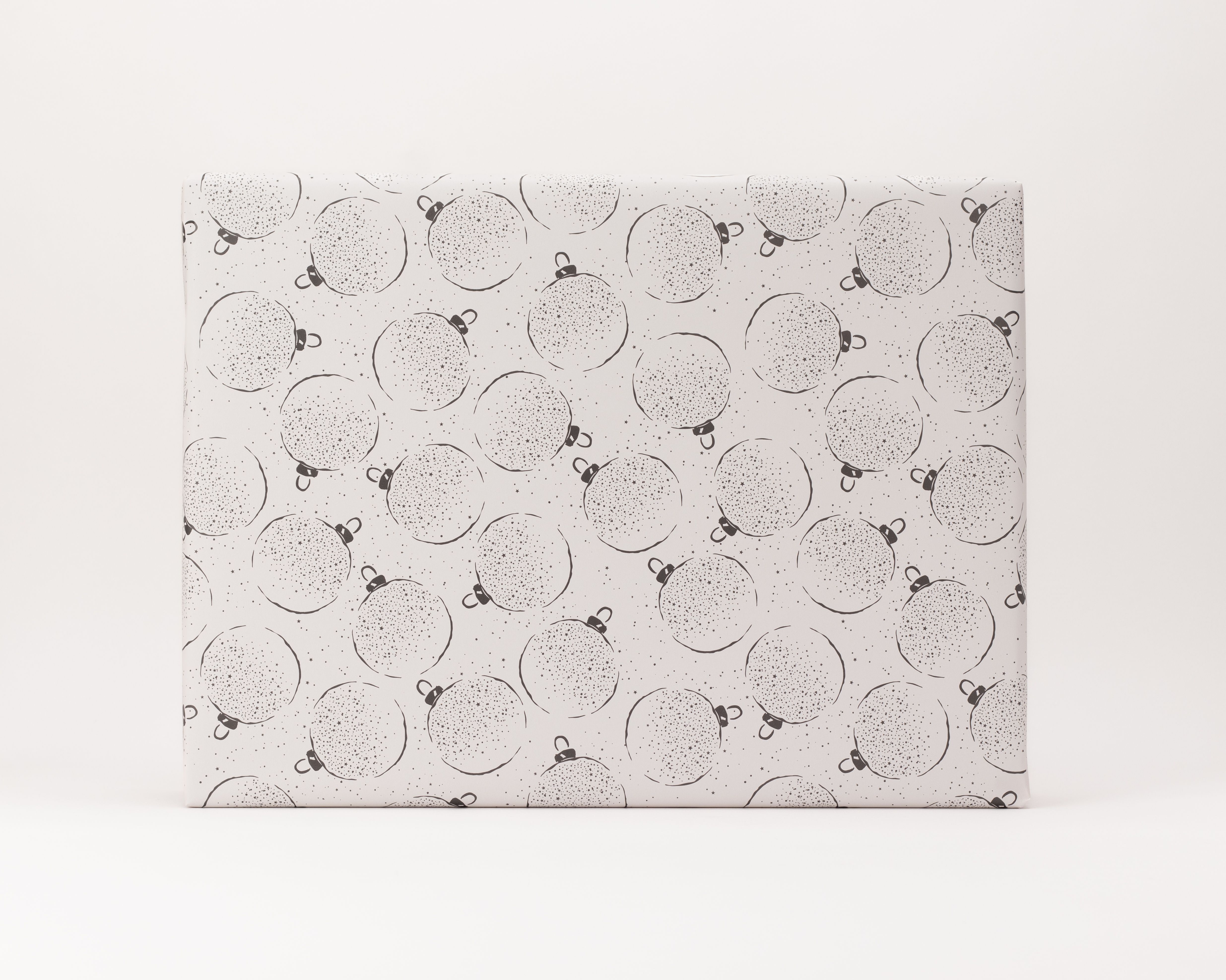 Geschenkpapier-Set mit einer Rolle auf hellem grauen Hintergrund, verziert mit dunkelgrauen, gepunkteten Weihnachtskugeln