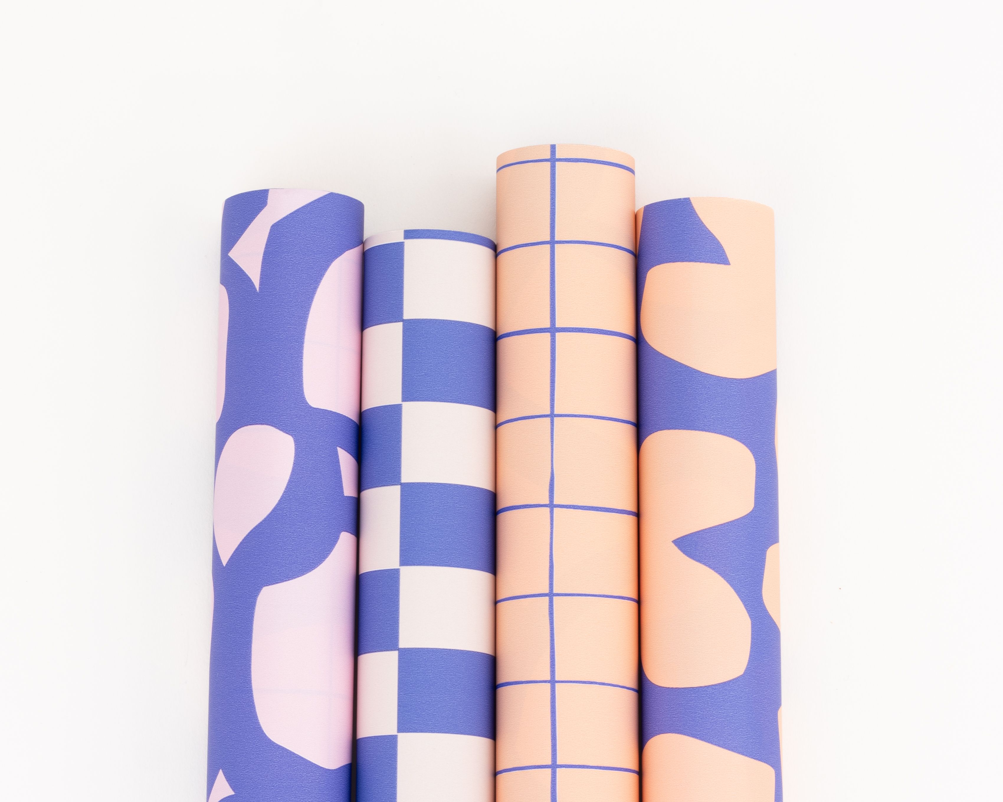 Geschenkpapier-Set mit vier Rollen. Die Papiere in Blau, Rosa, Pfirsich und Elfenbein zeigen grafische Muster wie abstrakte Formen, Schachbrett und Gitter