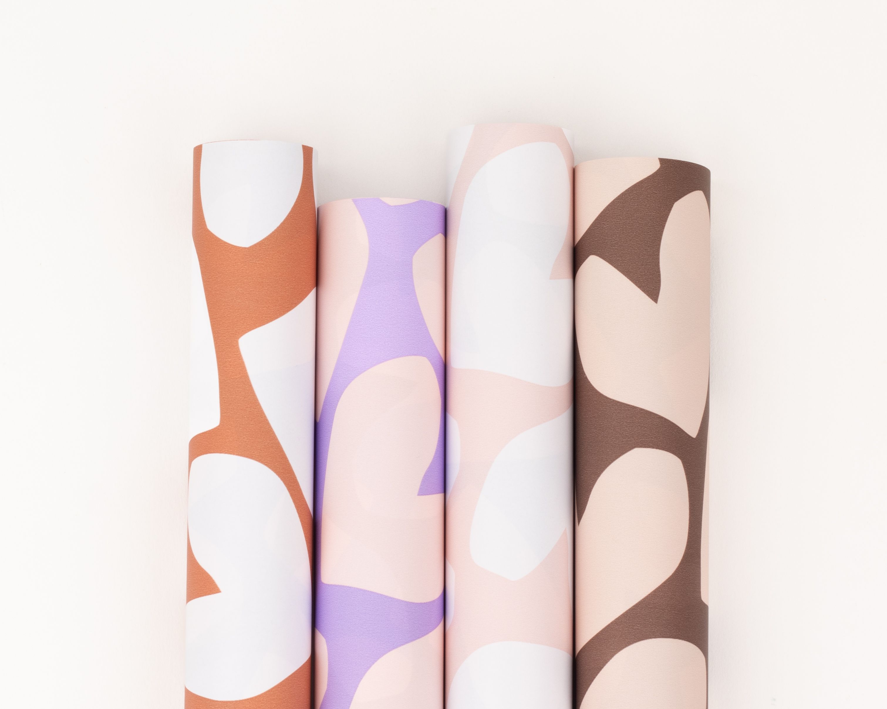 Geschenkpapier-Set mit vier Rollen, arrangiert nebeneinander, in den Farben Braun, Rost, Rosa, Flieder und Creme, jeweils mit abstraktem Herzmuster