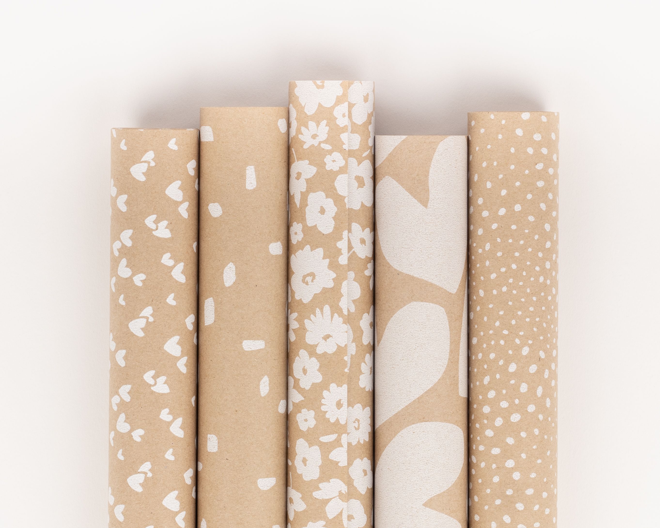 Geschenkpapier-Set mit fünf Rollen aus Kraftpapier mit verschiedenen weißen Mustern wie Herzen und Punkten