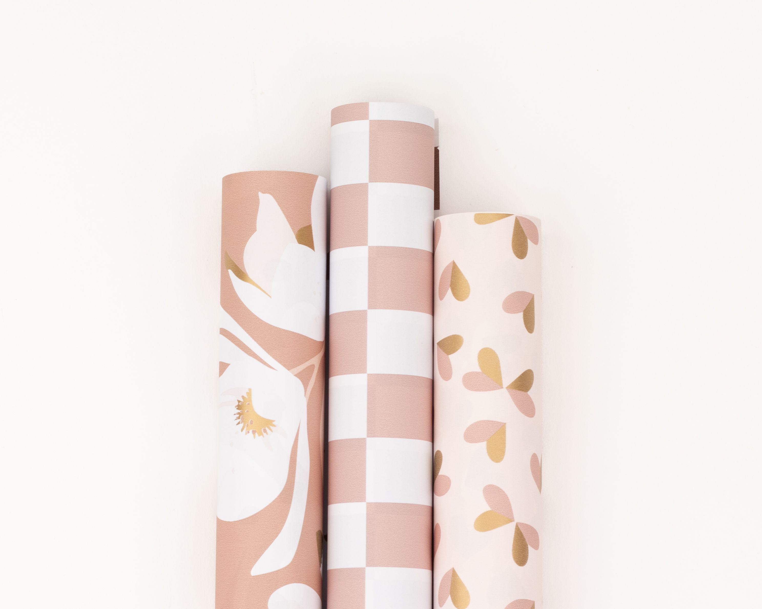 Geschenkpapier-Set mit drei nebeneinander liegenden Rollen in Rosa-, Gold- und Cremetönen, mit Mustern aus Blumen, Streifen und Herzen