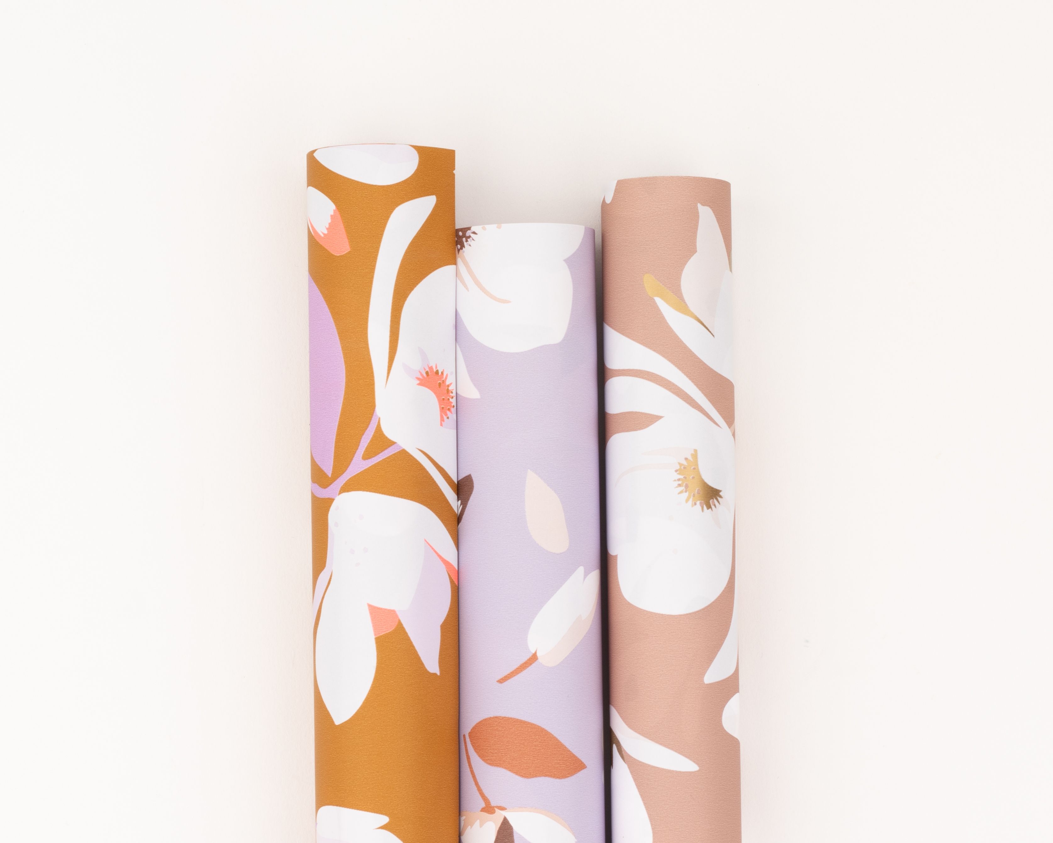 Geschenkpapier-Set mit drei nebeneinander liegenden Rollen und floralen Magnolienmustern in Rost, Flieder, Beige und Weiß