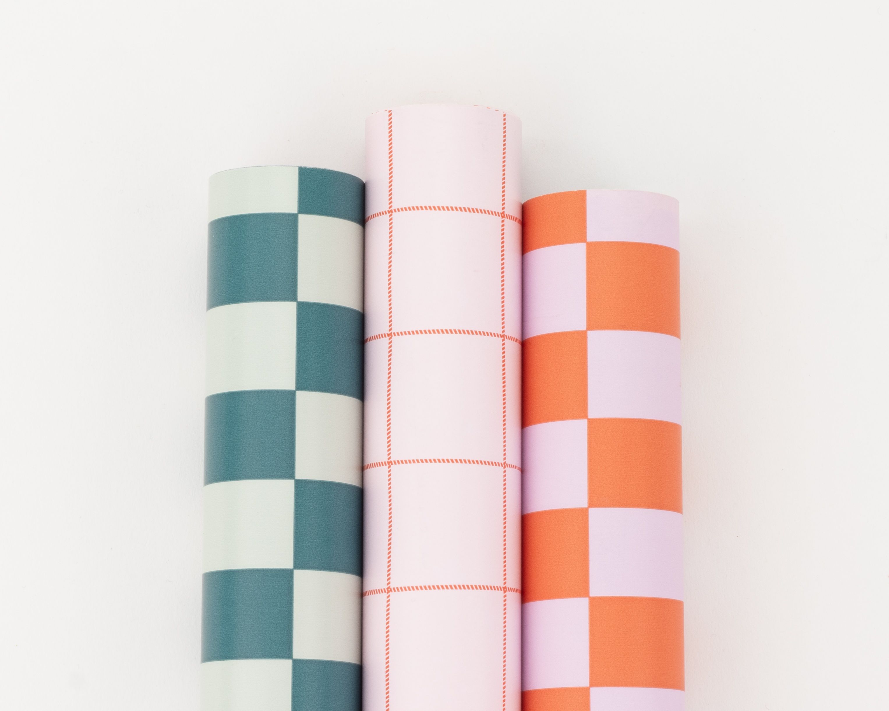 Geschenkpapier-Set mit drei nebeneinander liegenden Rollen in Blau, Rosa und Orangerot mit Blockstreifen und Gittermustern