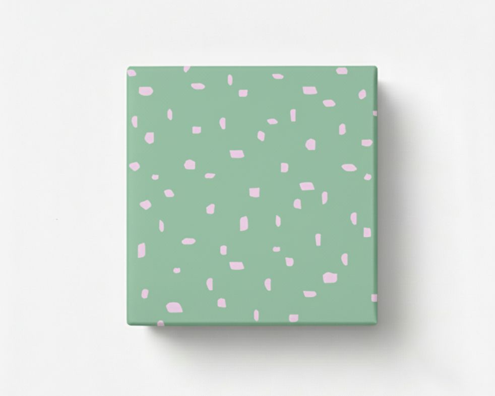 Geschenkpapier mit einem minimalistischen Muster aus unregelmäßigen rosa Flecken auf hellgrünem Grund, als verpacktes Geschenk präsentiert