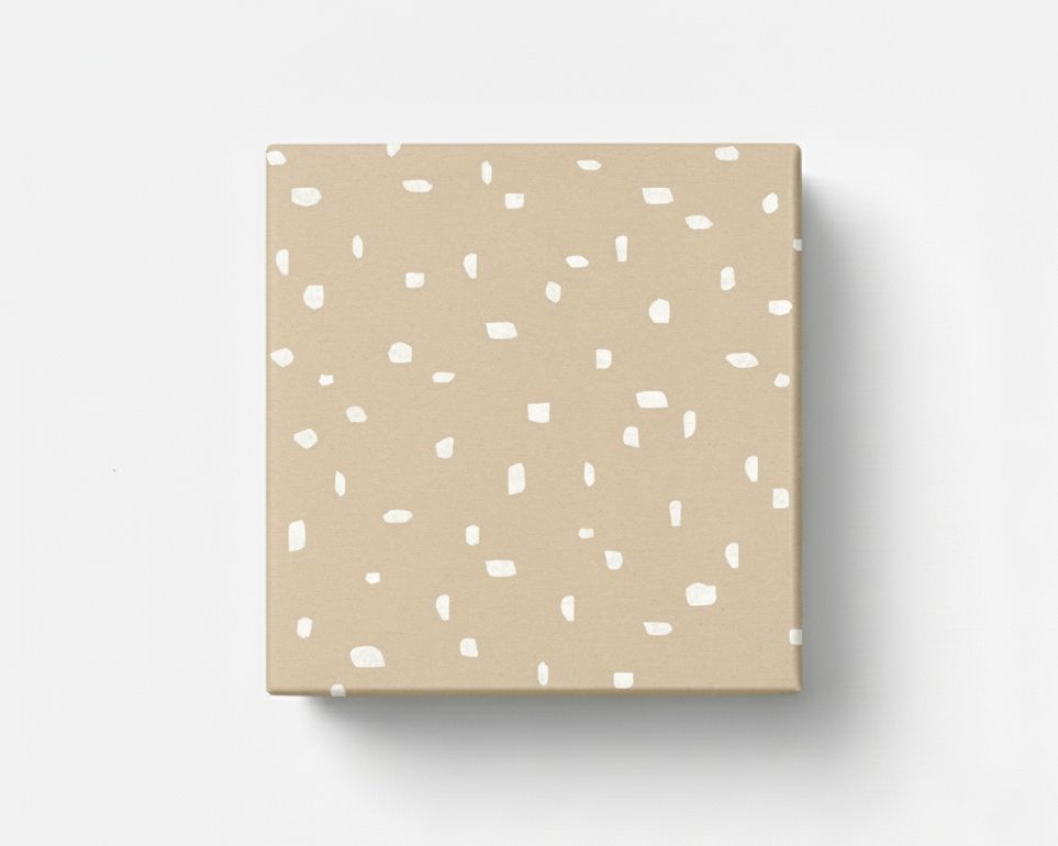Geschenkpapier mit unregelmäßigen weißen Punkten auf hellbraunem Kraftpapier, als verpacktes Geschenk von oben dargestellt