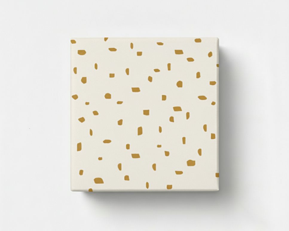 Geschenkpapier mit einem Muster aus unregelmäßigen goldenen Flecken auf hellem, cremefarbenem Hintergrund, als verpacktes Geschenk gezeigt