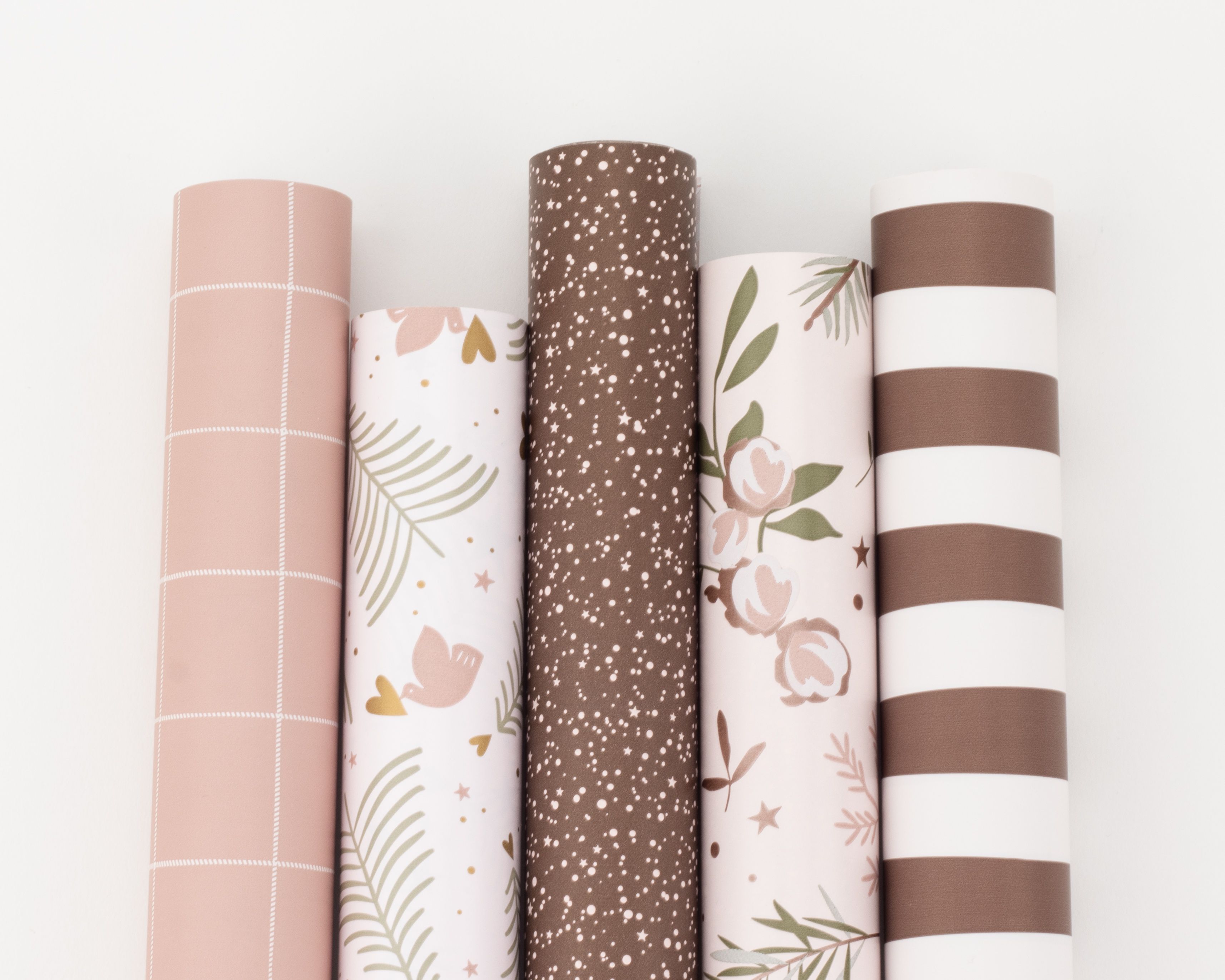 Geschenkpapier-Set mit fünf Rollen in Rosé-, Braun- und Grüntönen, mit Mustern wie Karos, Blumen, Sternen und Streifen nebeneinander liegend